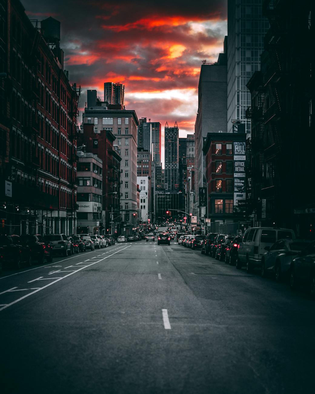 Moody city street with skyscrapers under a dramatic dusk sky.