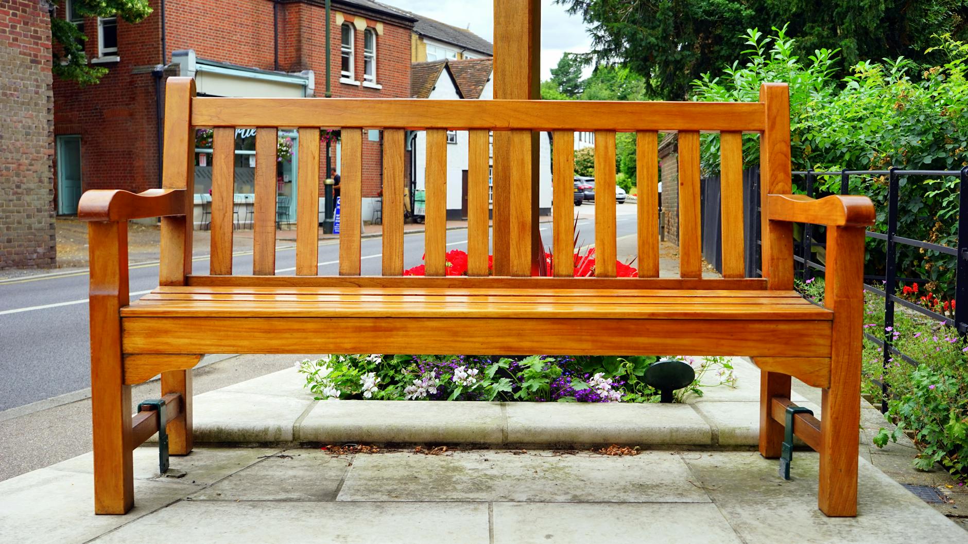 A wooden bench is placed in an urban street surrounded by vibrant flowers. A wooden bench is placed in an urban street surrounded by vibrant flowers.