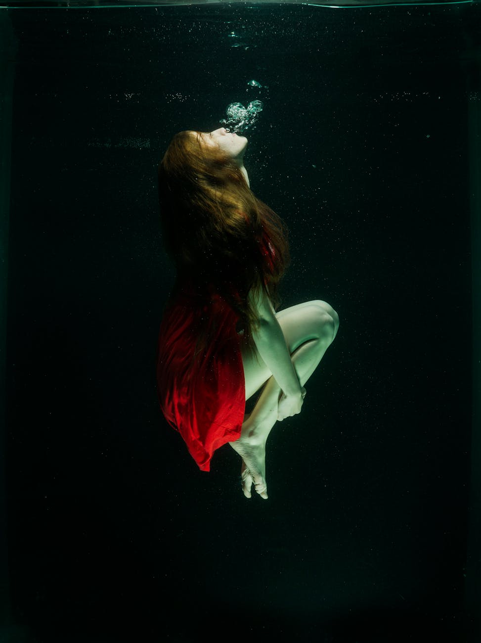 Woman in red dress captured gracefully underwater, creating an ethereal and artistic scene.