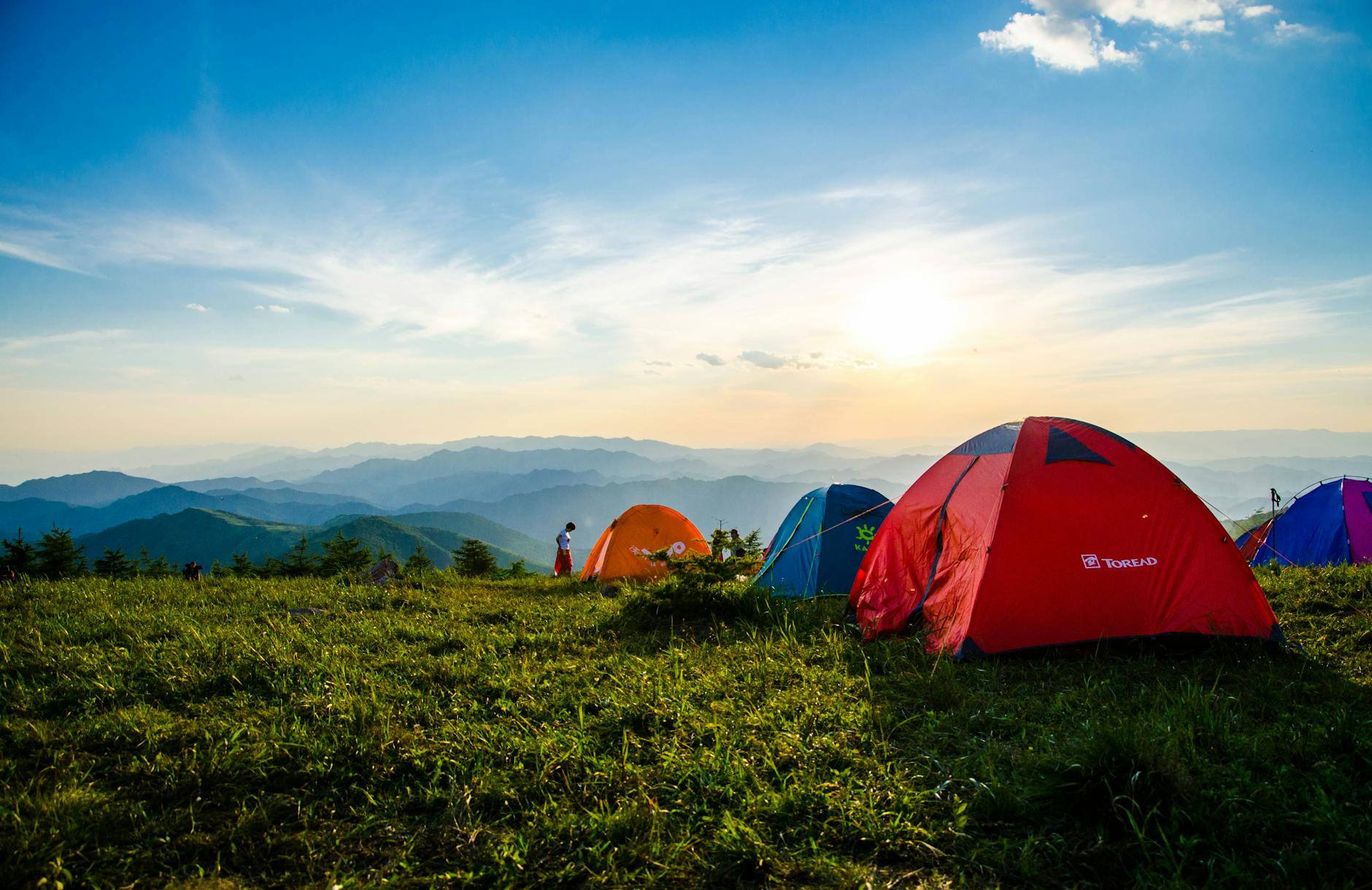 Vibrant tents on a grassy mountain ridge with a stunning sunrise view, ideal for adventure. Vibrant tents on a grassy mountain ridge with a stunning sunrise view, ideal for adventure.