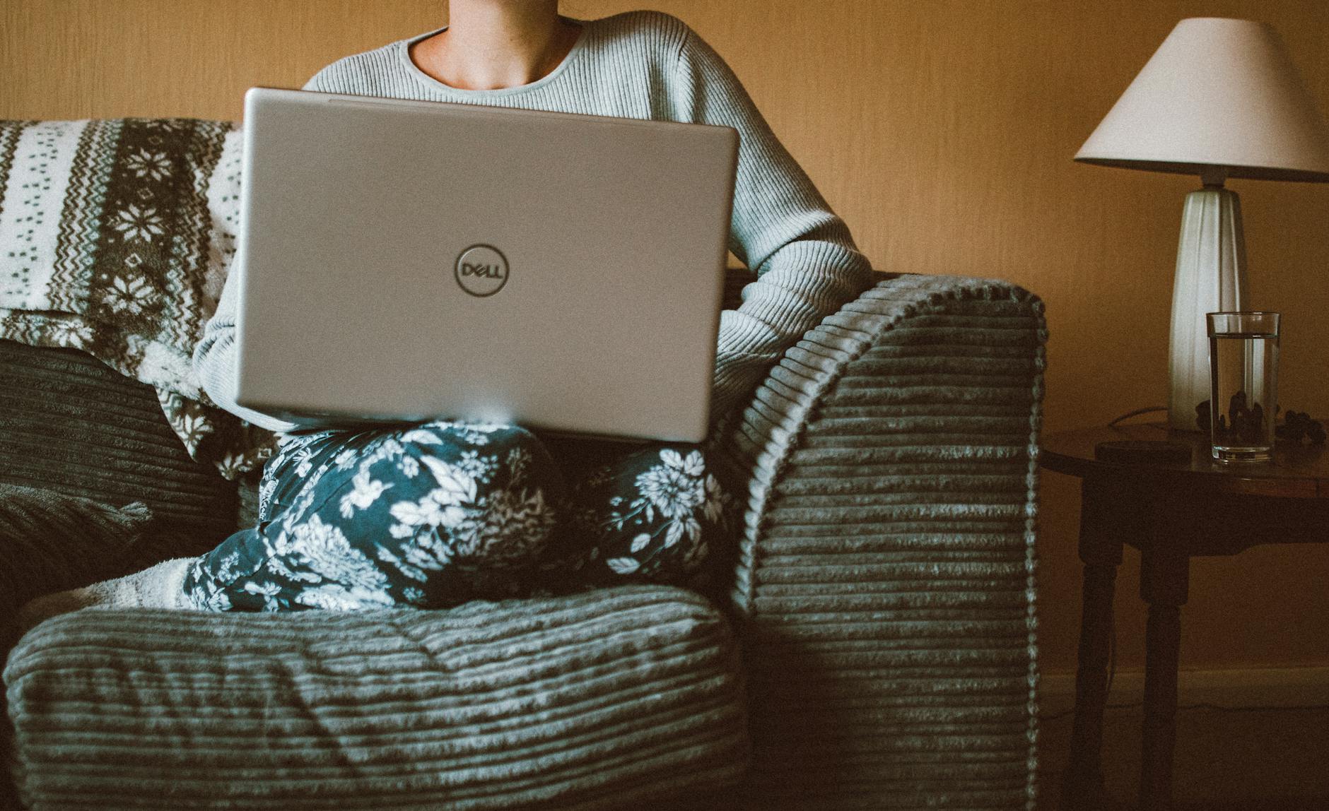 A woman in casual clothing works on a laptop while relaxing on a cozy sofa indoors. A woman in casual clothing works on a laptop while relaxing on a cozy sofa indoors.