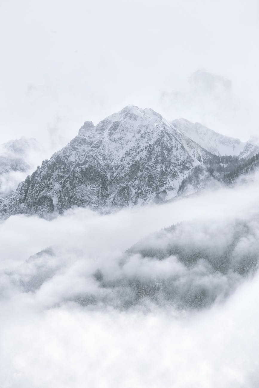 Breathtaking winter scene of a snow-covered mountain peak surrounded by misty clouds.