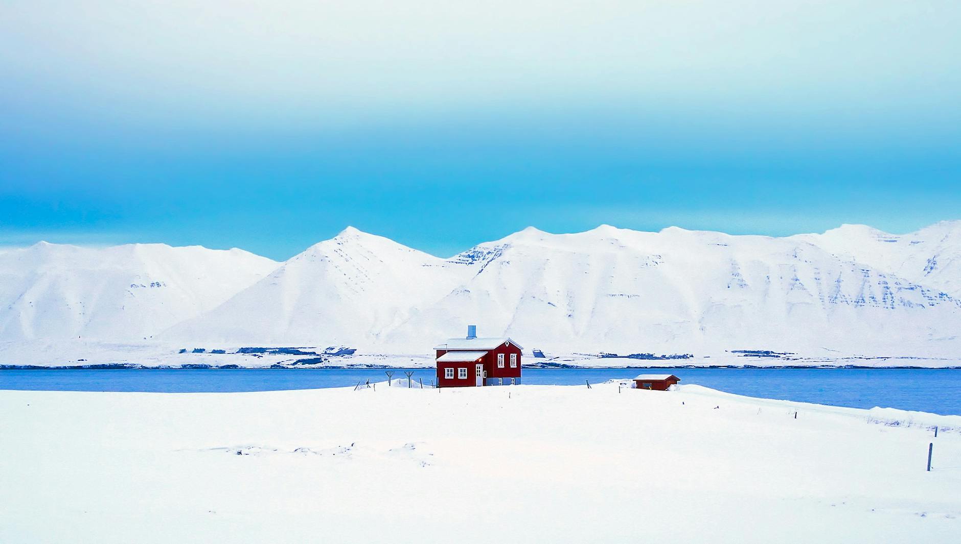 A solitary red cabin amidst a vast snowy landscape with blue sky in Iceland, capturing winter’s beauty. A solitary red cabin amidst a vast snowy landscape with blue sky in Iceland, capturing winter’s beauty.