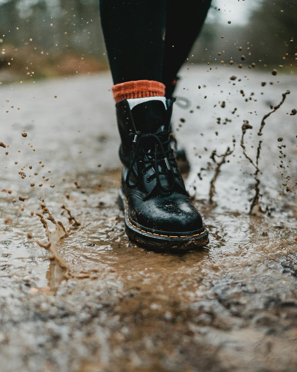Focus on black boots splashing in a muddy puddle on a rainy day, highlighting fashion and adventure. Focus on black boots splashing in a muddy puddle on a rainy day, highlighting fashion and adventure.