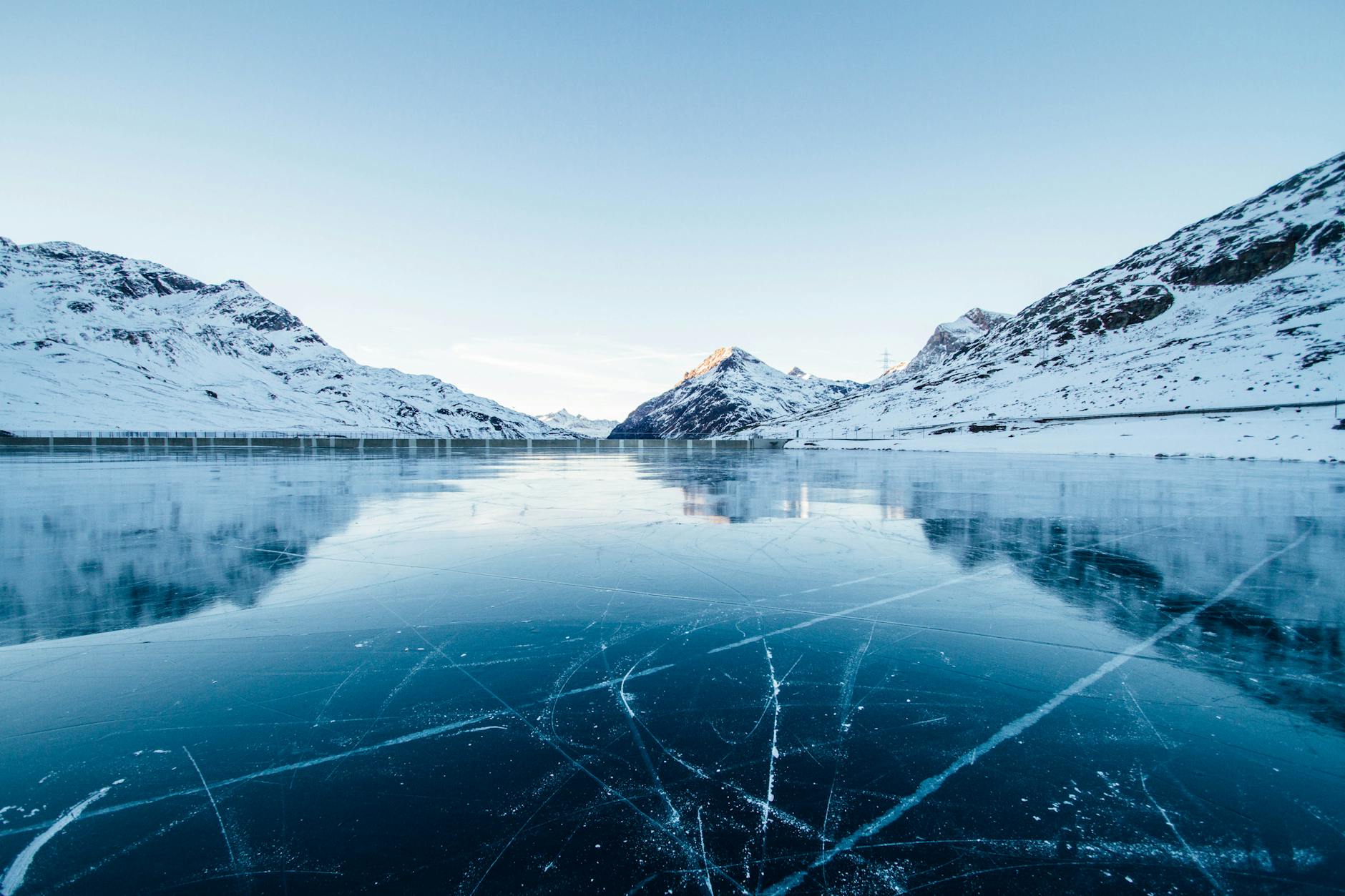 A serene winter landscape featuring a frozen lake surrounded by snow-covered mountains in Switzerland.