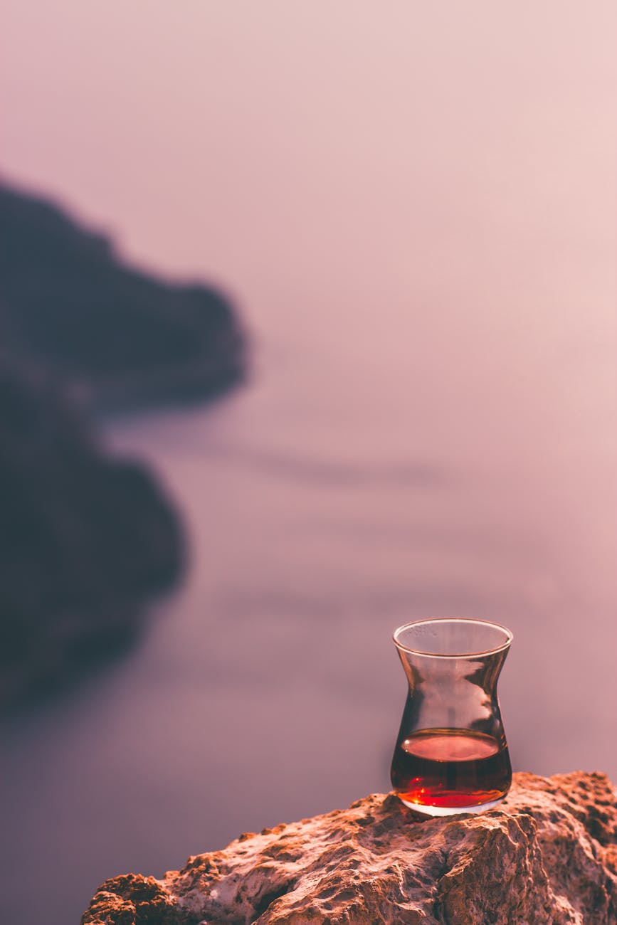 Glass of red tea on rocky cliff with a sunset coastal view. Tranquil and serene.