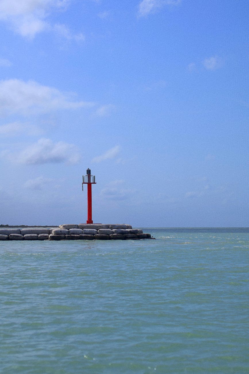 Peaceful coastal scene with a solitary red lighthouse on a calm sea under a clear blue sky. Peaceful coastal scene with a solitary red lighthouse on a calm sea under a clear blue sky.