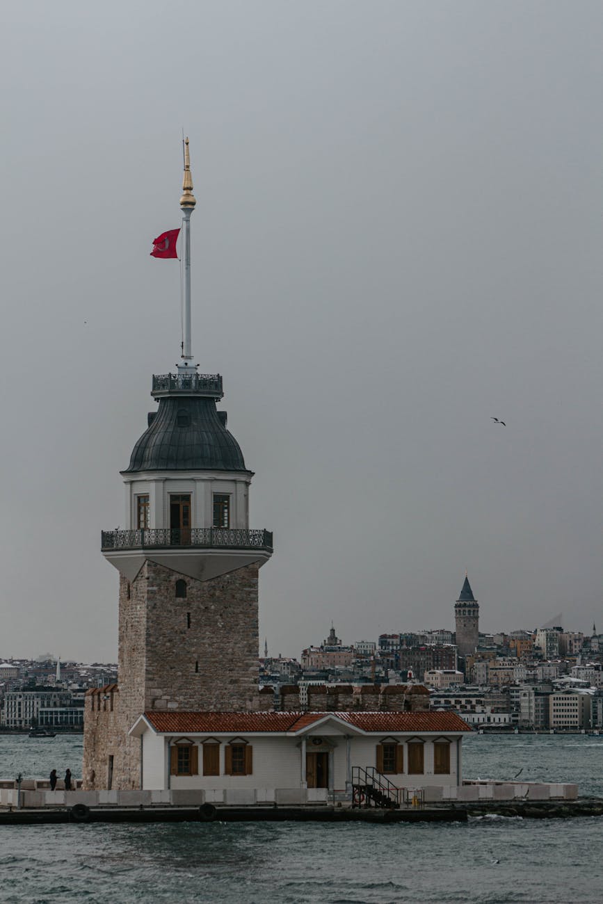 View of Istanbul’s iconic Maiden’s Tower with the city skyline in the background under overcast weather. View of Istanbul’s iconic Maiden’s Tower with the city skyline in the background under overcast weather.