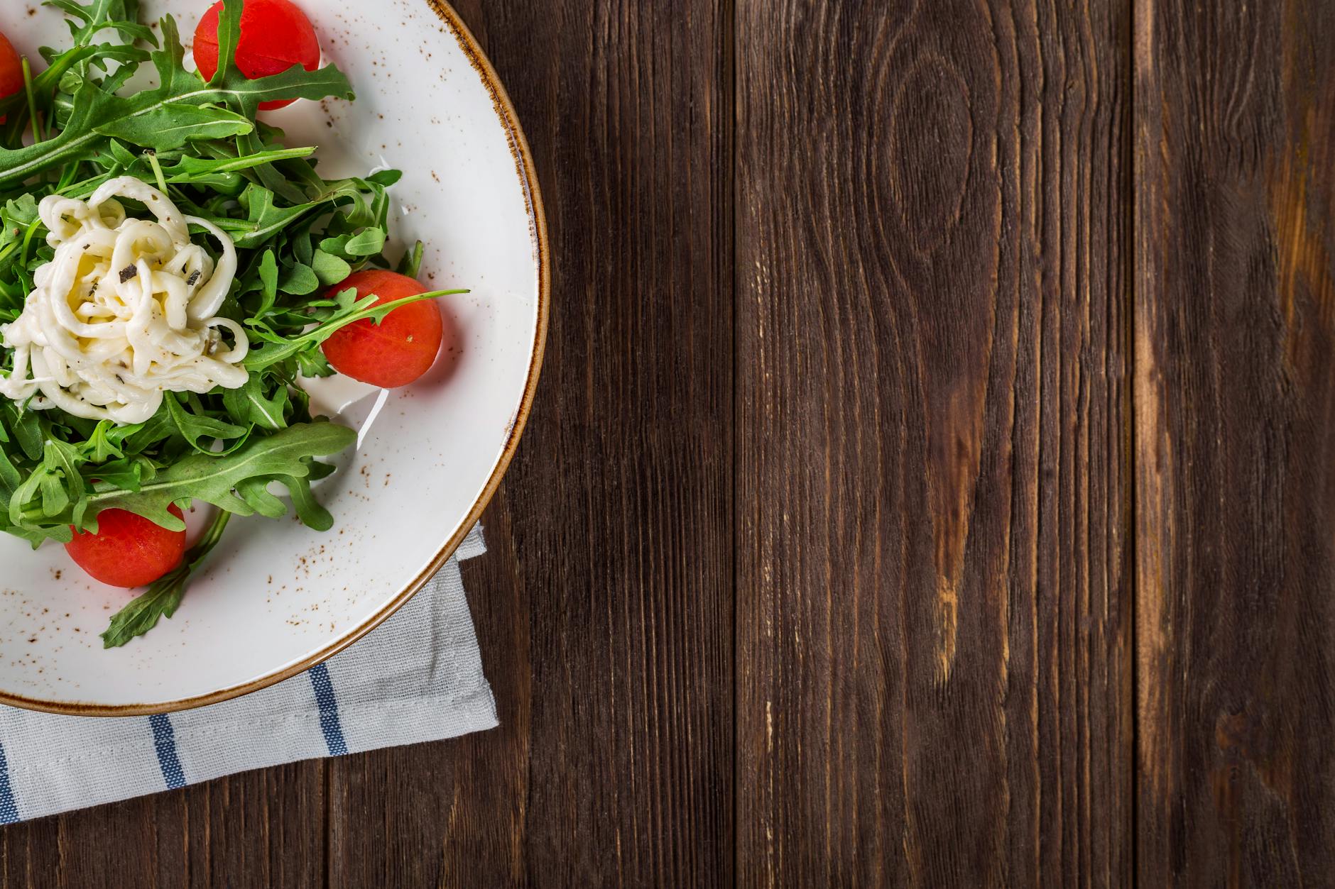 A delightful arugula salad with tomatoes and cheese, served on a rustic wooden table, perfect for healthy eating. A delightful arugula salad with tomatoes and cheese, served on a rustic wooden table, perfect for healthy eating.