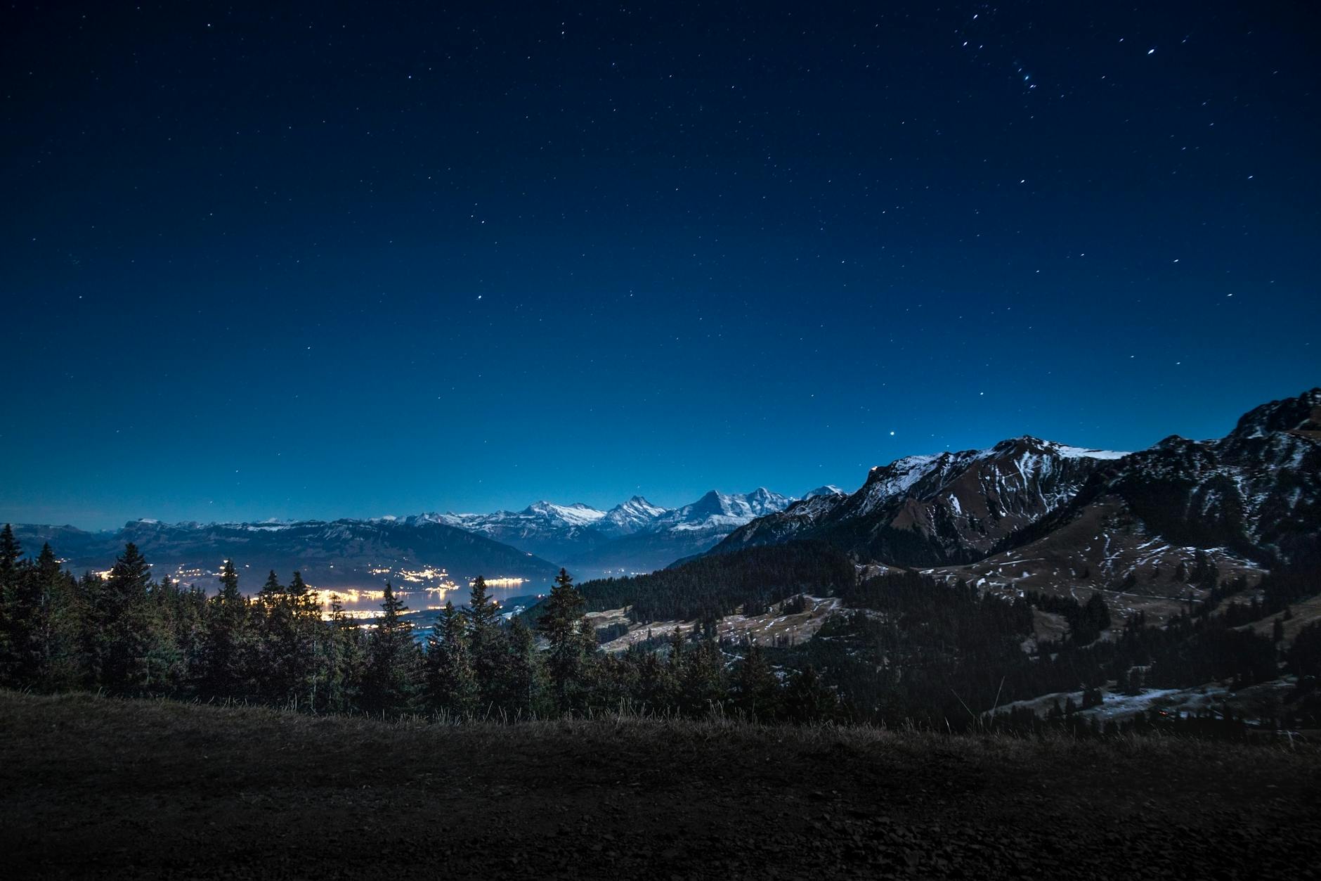 Captivating starry night overlooking illuminated town and mountainous backdrop.
