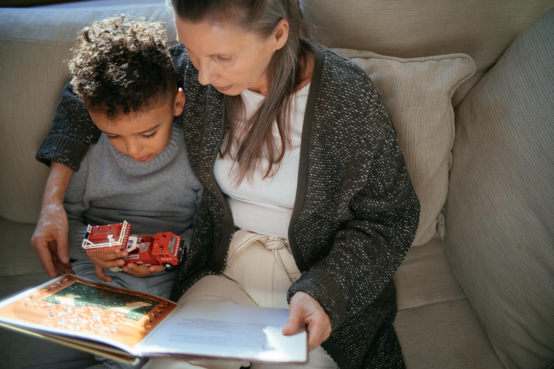 A grandmother and grandson sharing a cozy reading moment on a sofa indoors. A grandmother and grandson sharing a cozy reading moment on a sofa indoors.