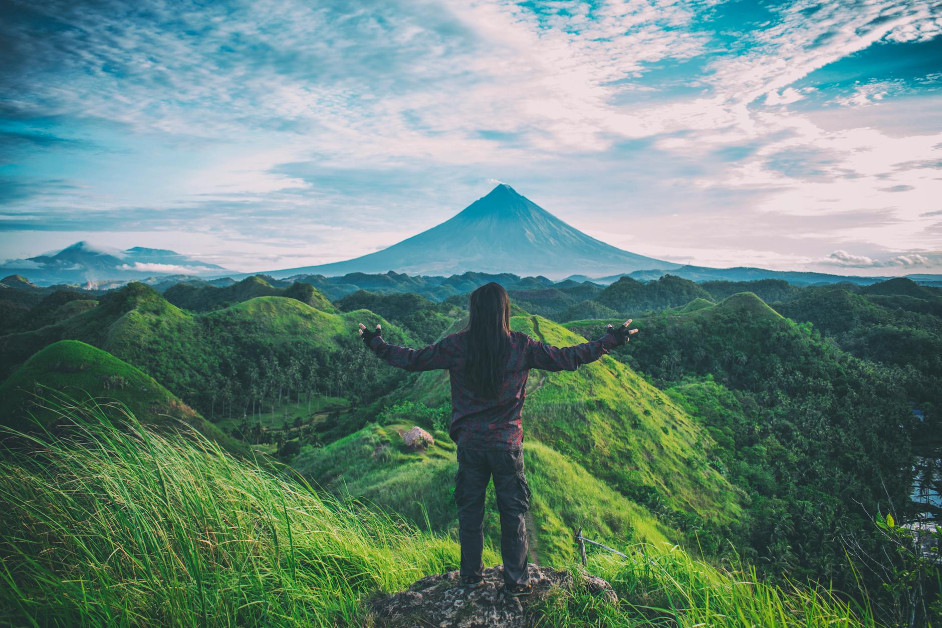 A person enjoys an expansive view of Mt. Mayon amidst lush green hills in Bicol, Philippines. A person enjoys an expansive view of Mt. Mayon amidst lush green hills in Bicol, Philippines.