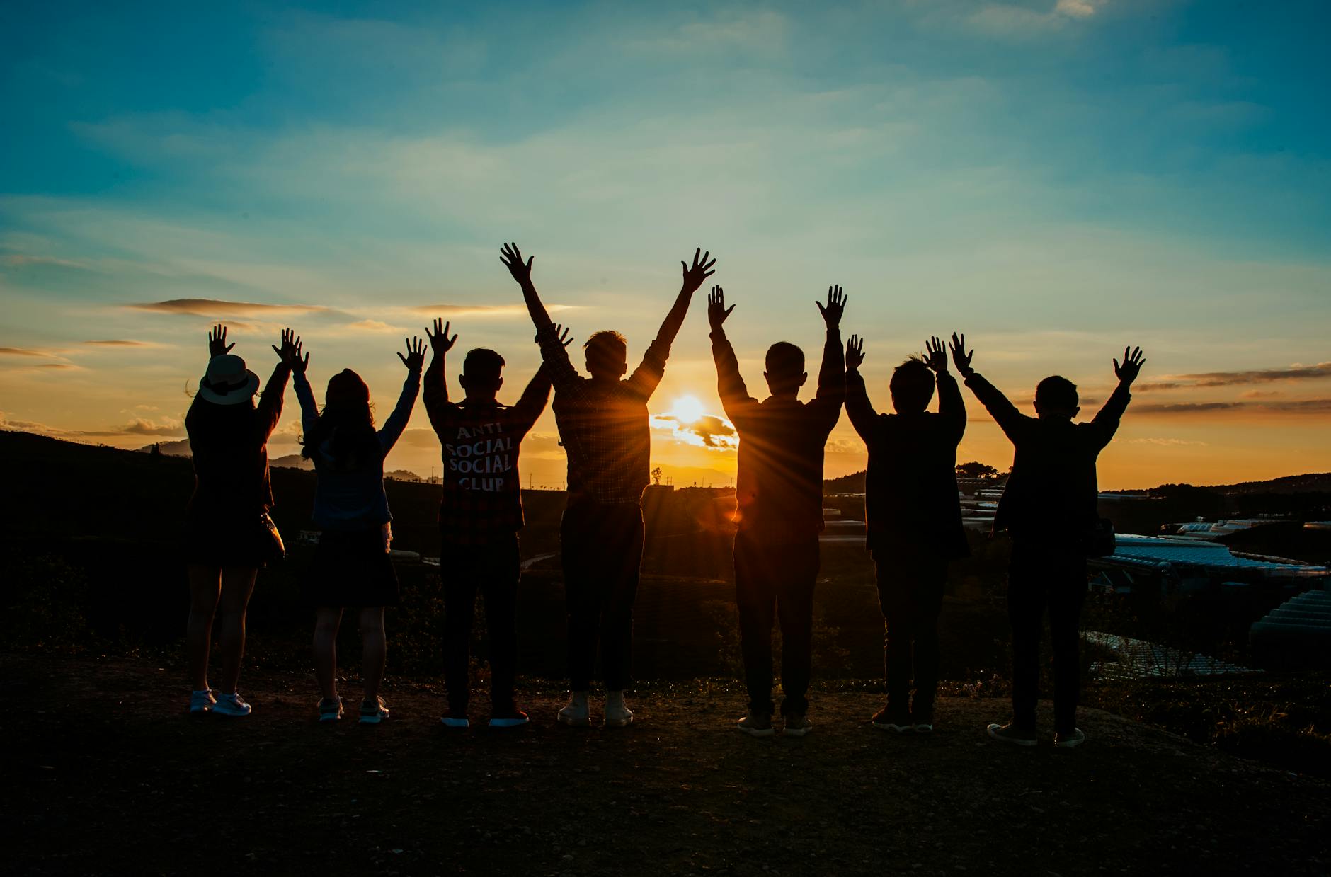 A diverse group of friends raises their arms in celebration against a vibrant sunset backdrop. A diverse group of friends raises their arms in celebration against a vibrant sunset backdrop.