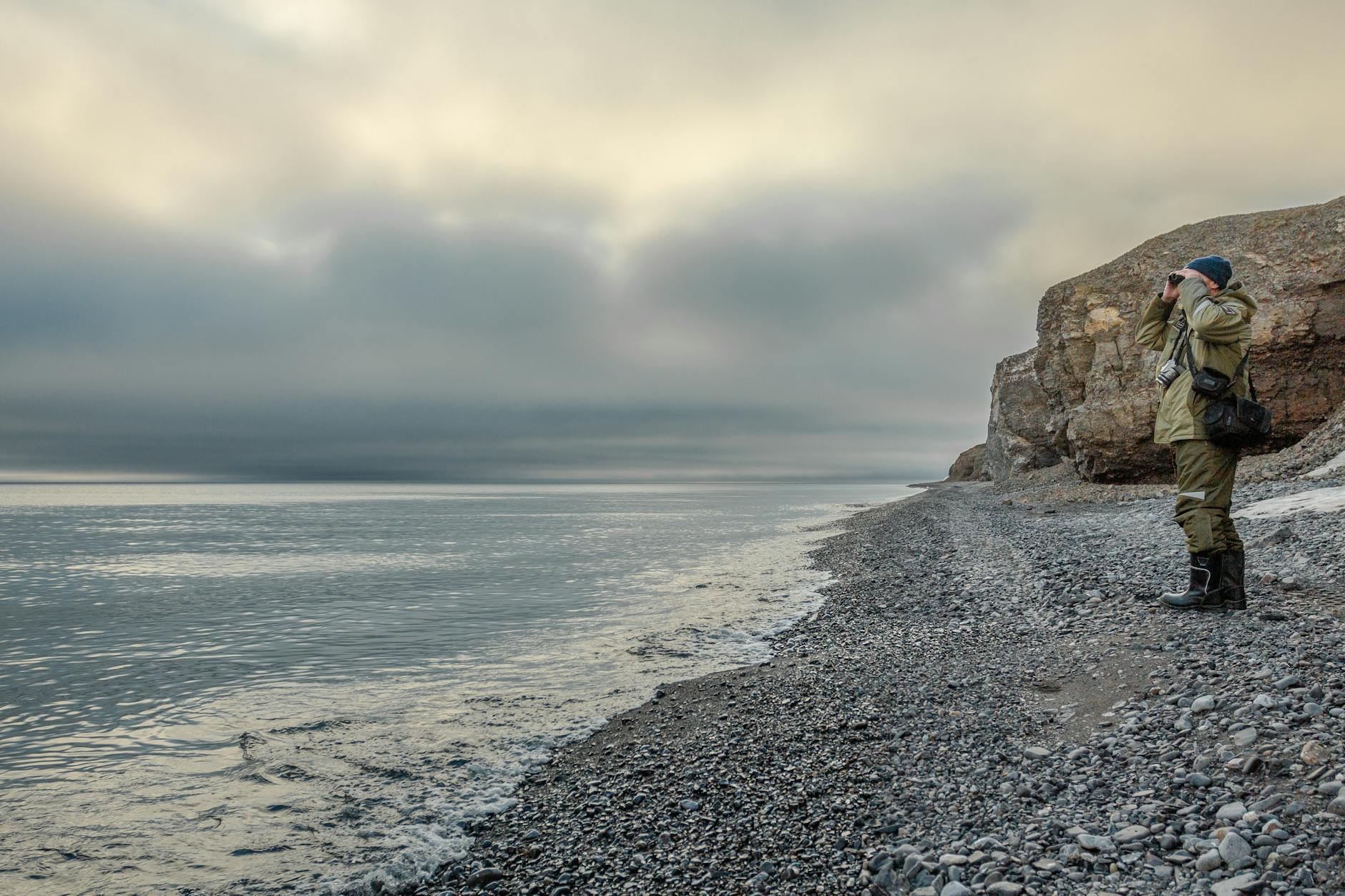 Photographer exploring a rocky coastal landscape under a moody sky.
