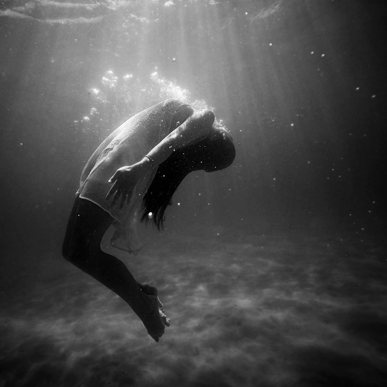 A woman underwater in a dramatic, black and white photographic capture, embodying grace and mystery.