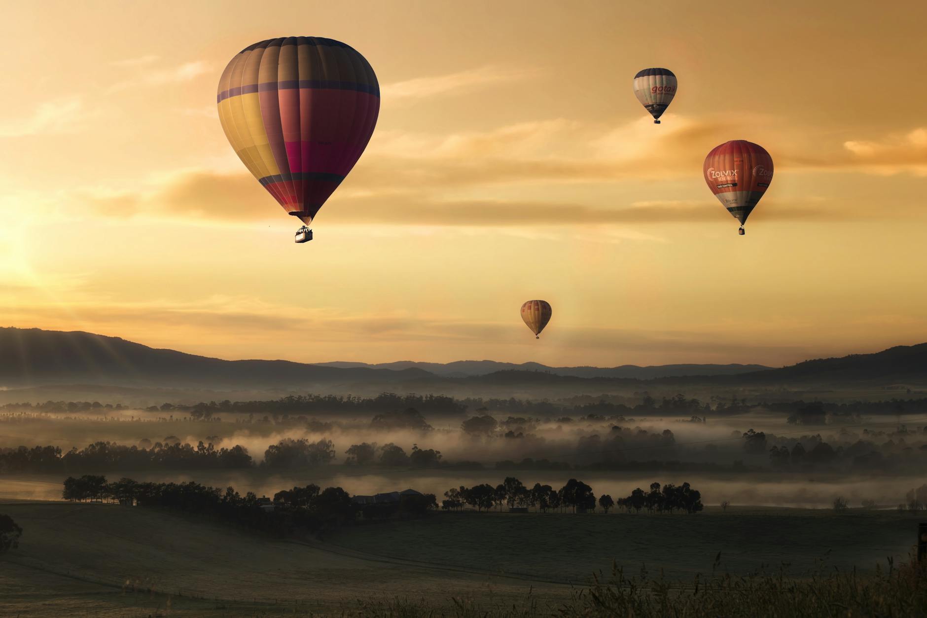 Hot air balloons floating over misty fields at sunrise, creating a picturesque adventure scene. Hot air balloons floating over misty fields at sunrise, creating a picturesque adventure scene.