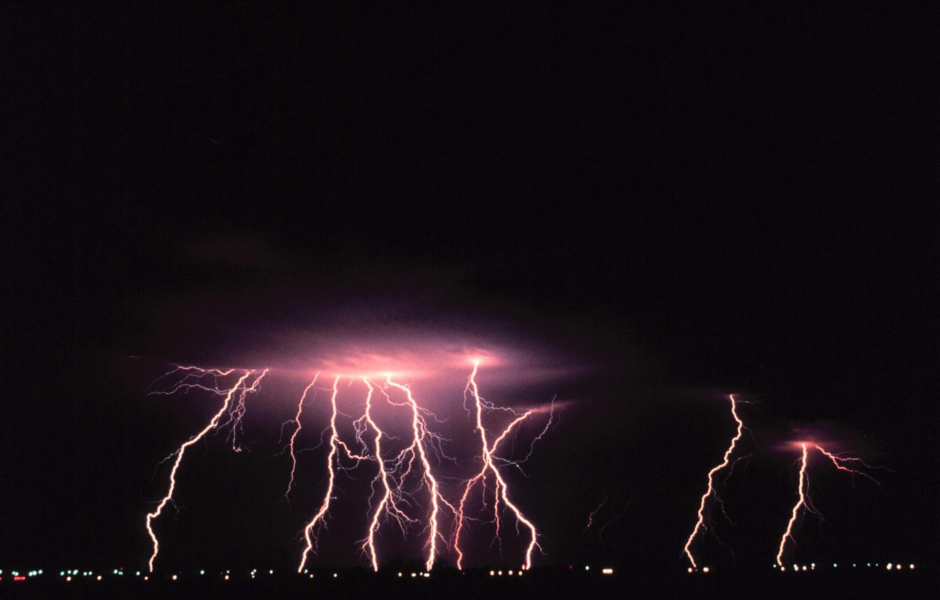 A striking display of lightning illuminating the night sky over a city landscape.