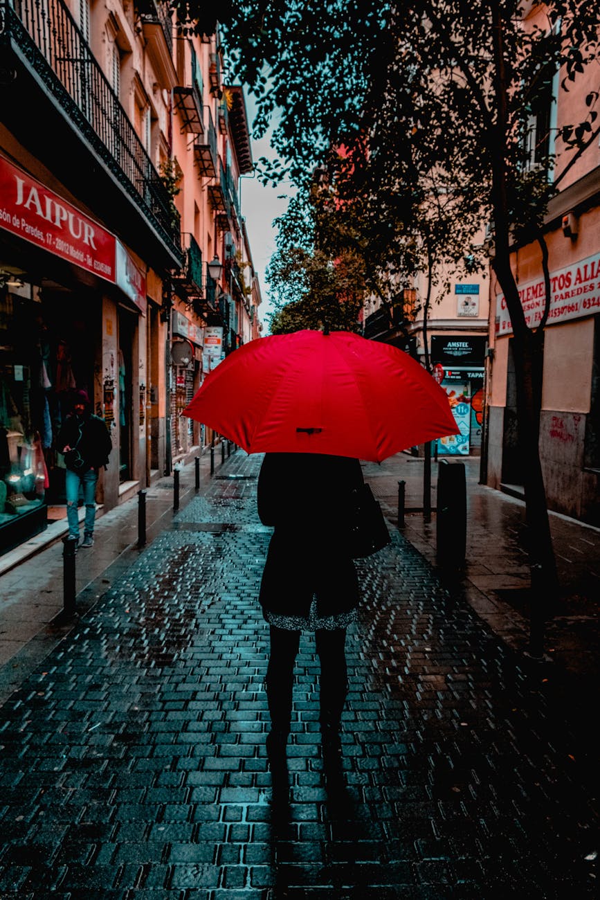 A person with a red umbrella walking on a rainy street in Madrid, Spain.