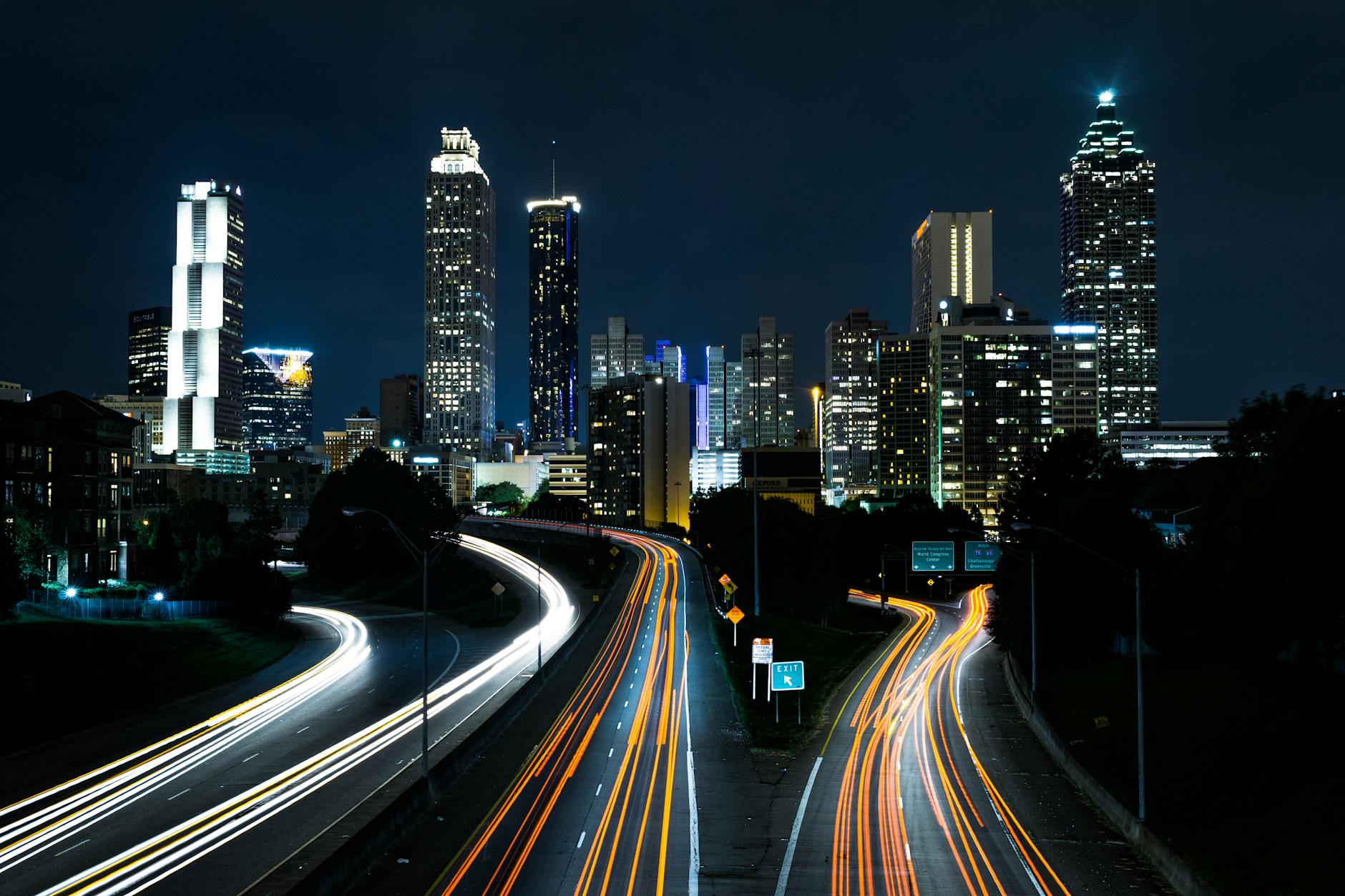 A vibrant cityscape at night showcasing light trails on the highway beneath towering skyscrapers.