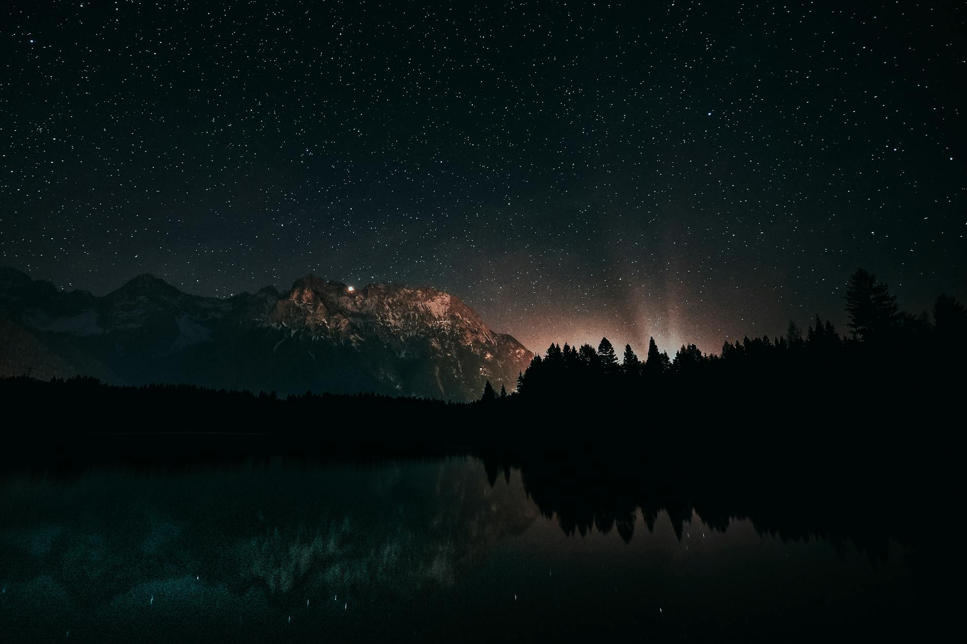 Beautiful starry night with mountains and forest reflecting on calm water