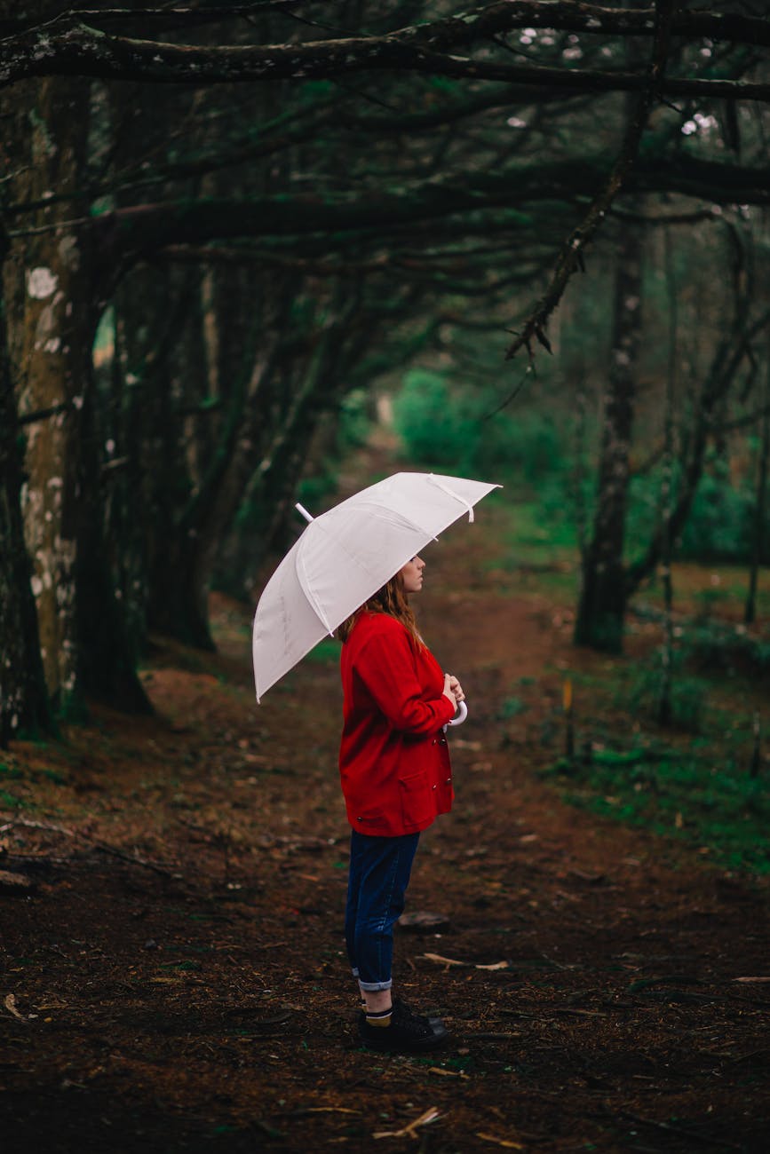 Woman standing with umbrella in a gloomy forest pathway, evoking a sense of solitude and contemplation. Woman standing with umbrella in a gloomy forest pathway, evoking a sense of solitude and contemplation.