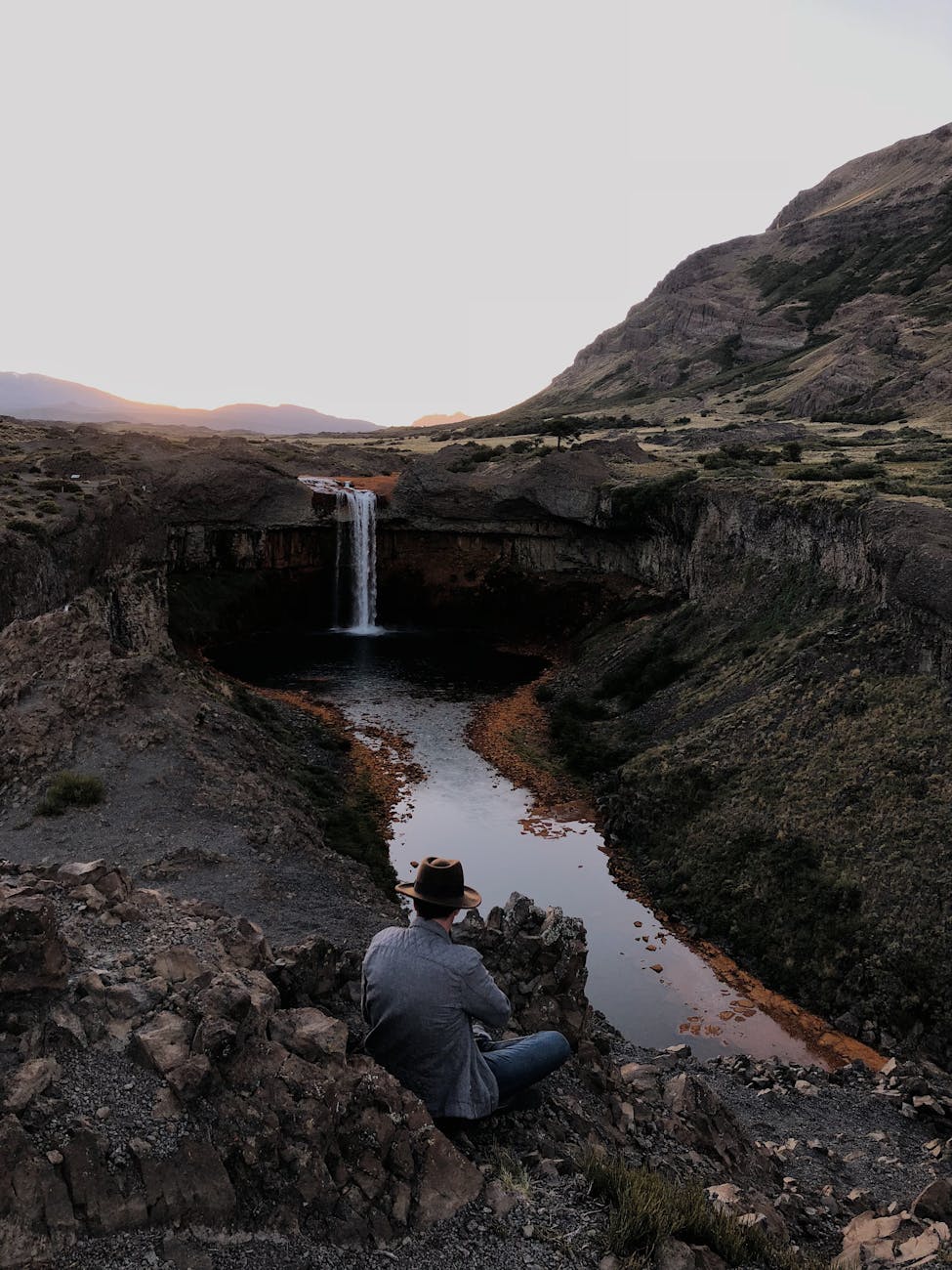 A lone traveler by a waterfall, surrounded by a dramatic landscape.