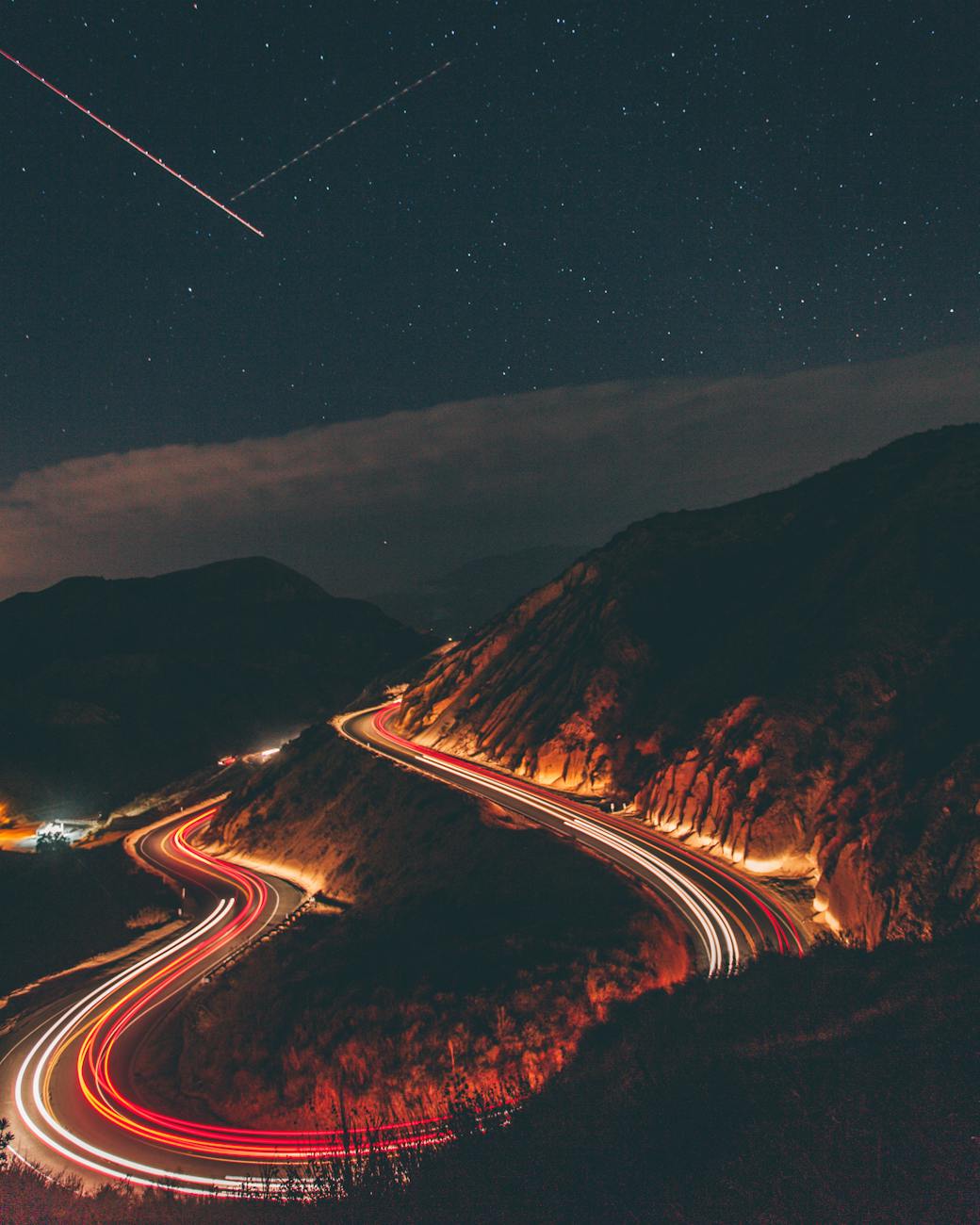 A captivating long exposure shot of a winding highway at night with car light trails under a starry sky. A captivating long exposure shot of a winding highway at night with car light trails under a starry sky.