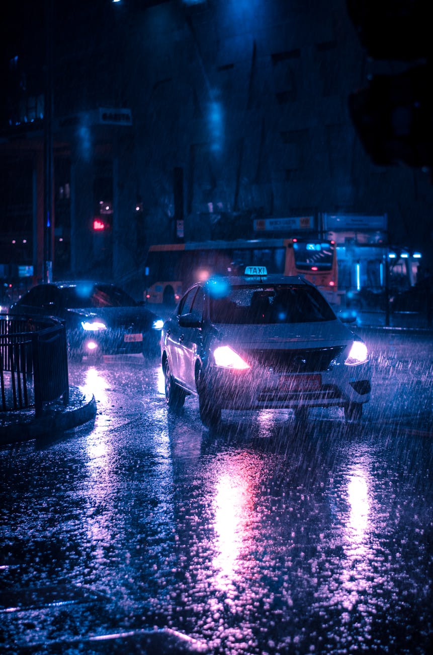 Urban street at night with cars in heavy rain, reflecting neon lights.