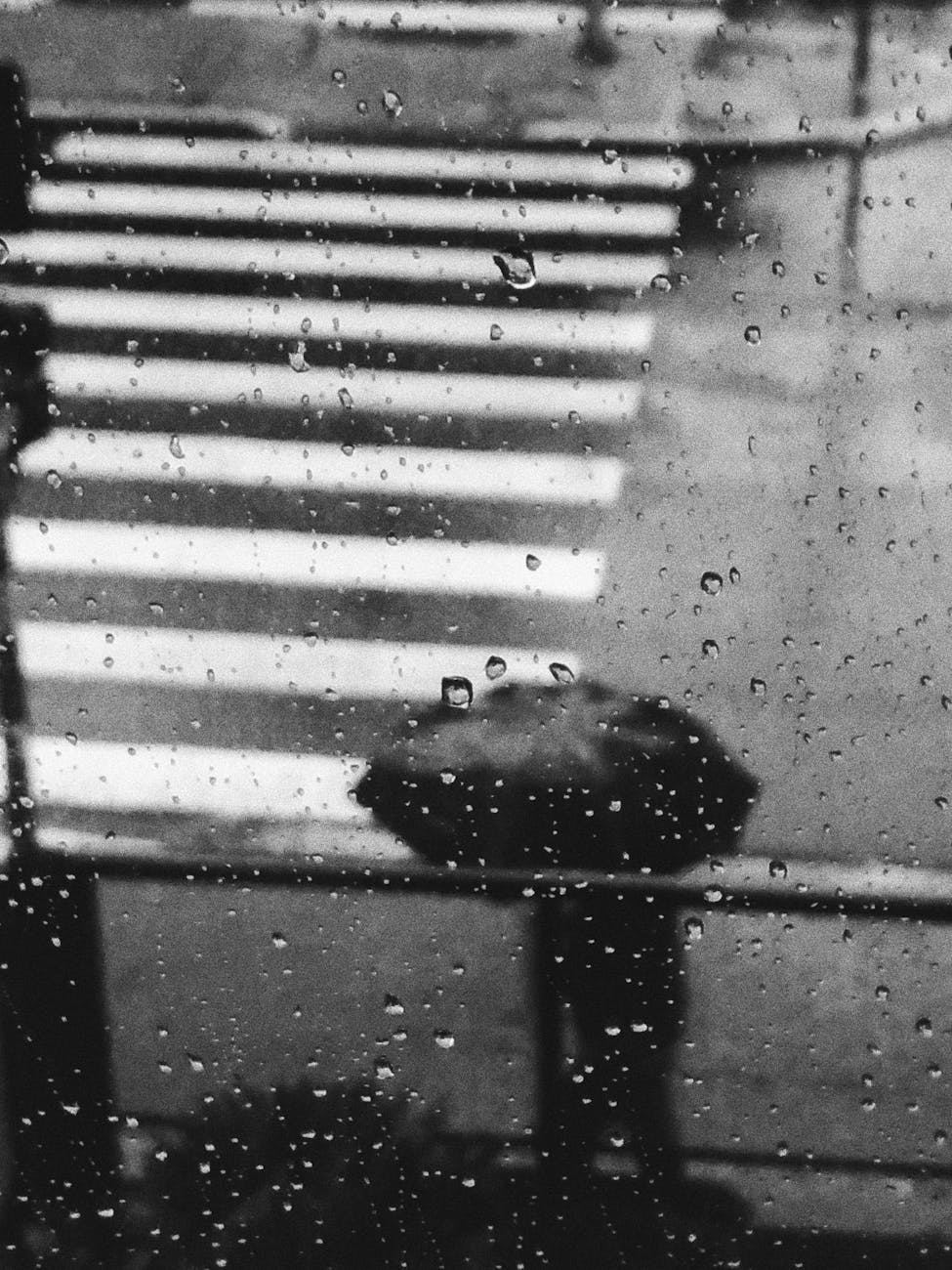 Monochrome view of raindrops on glass with a figure holding an umbrella in the background. Monochrome view of raindrops on glass with a figure holding an umbrella in the background.