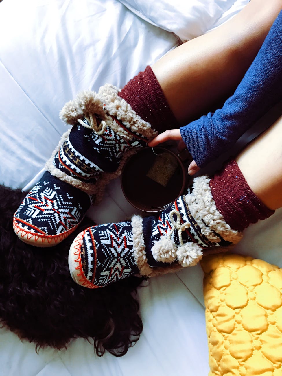 Top view of cozy woolen slippers and a warm drink on a bed, perfect for winter mornings.