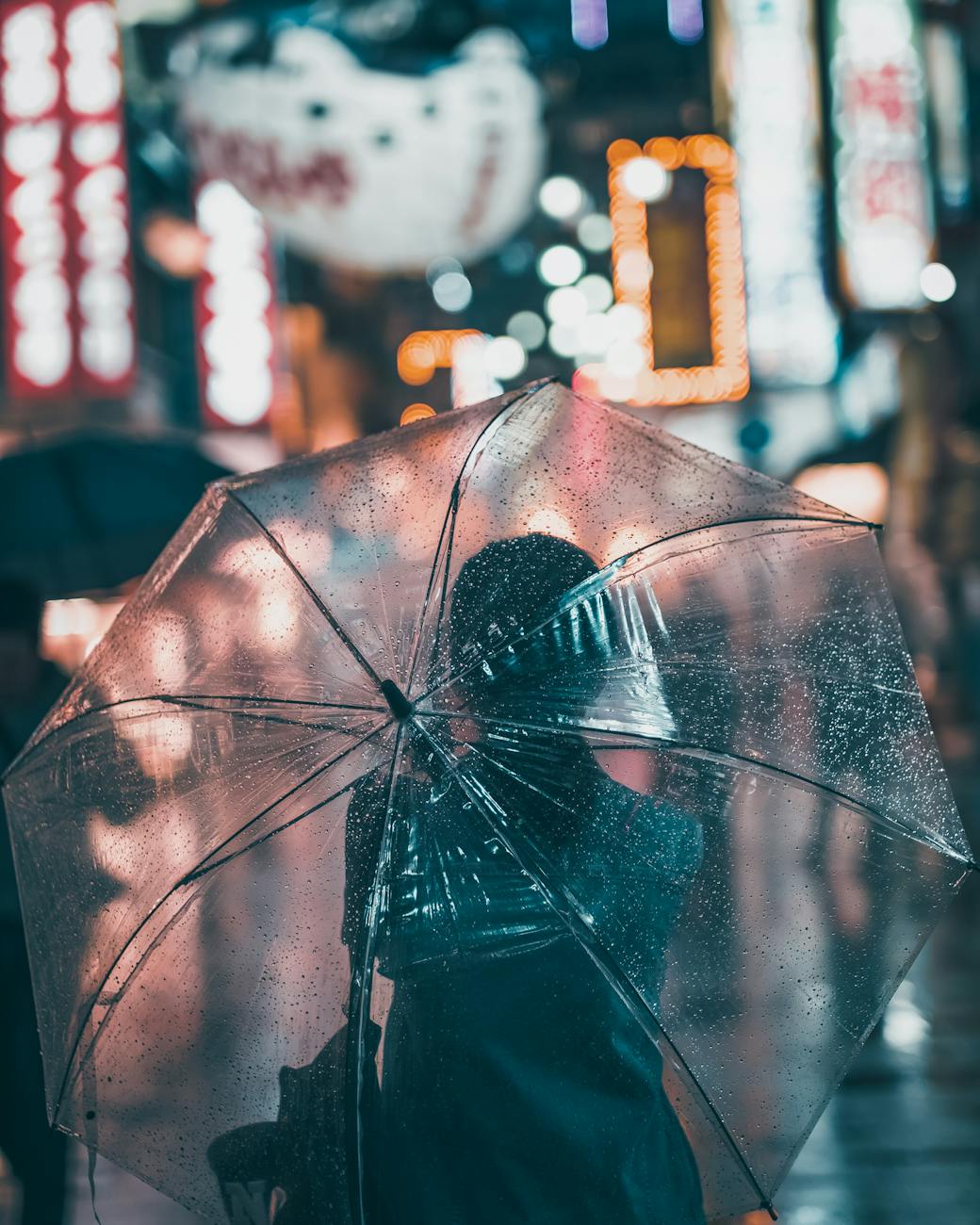 A person with an umbrella walks through a bustling, rainy street in Osaka at night.