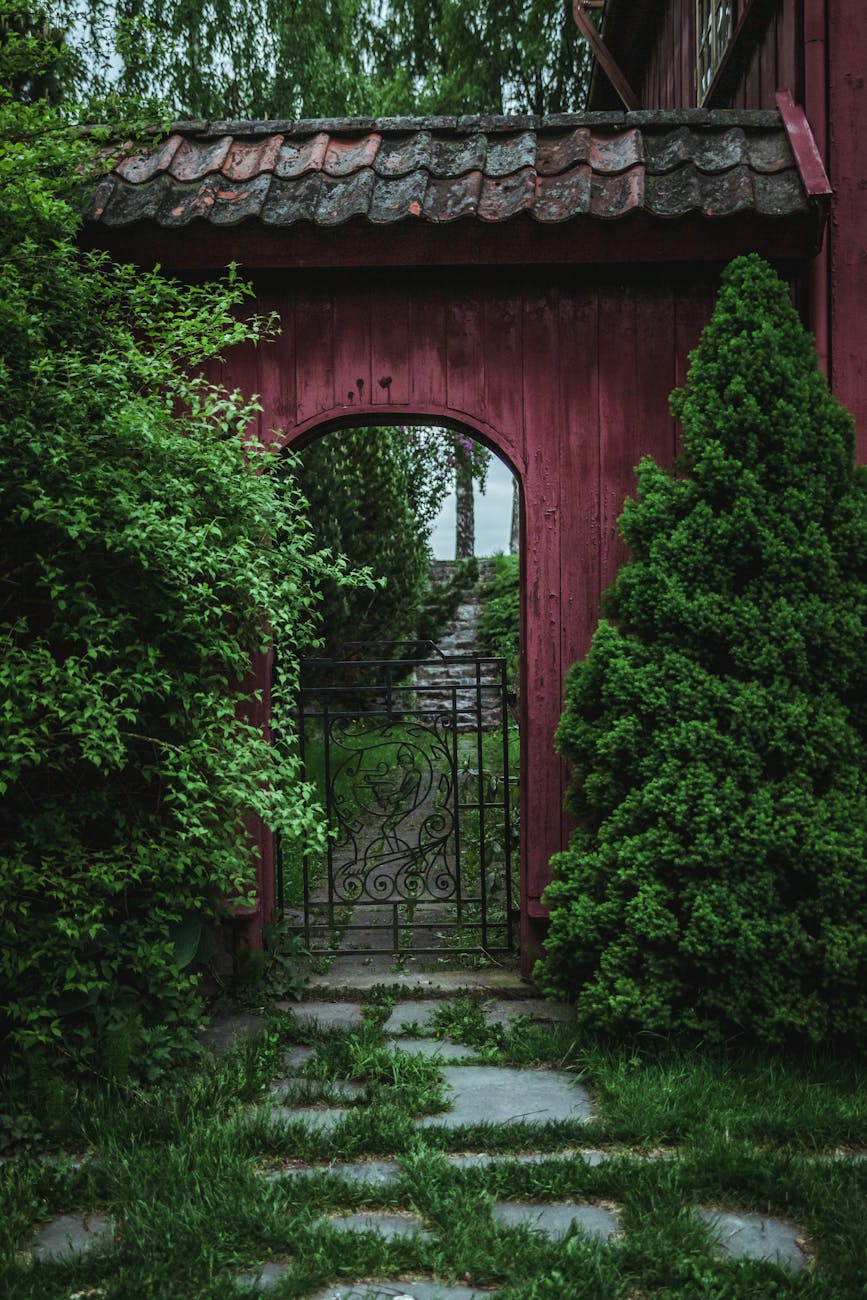 Rustic red garden gate surrounded by lush green foliage in a tranquil setting in Oslo.