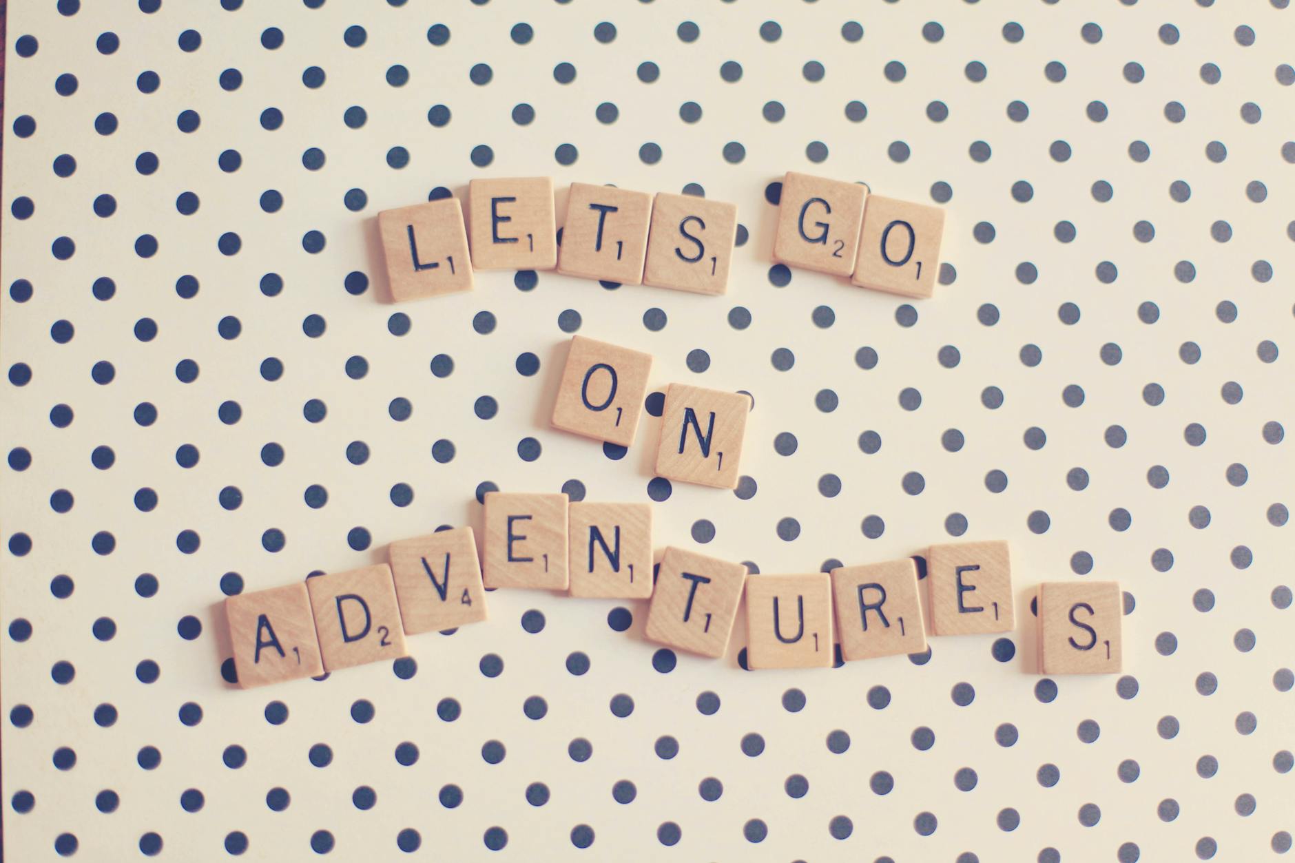 Scrabble tiles spell ‘Let’s go on adventures’ on a polka dot background.