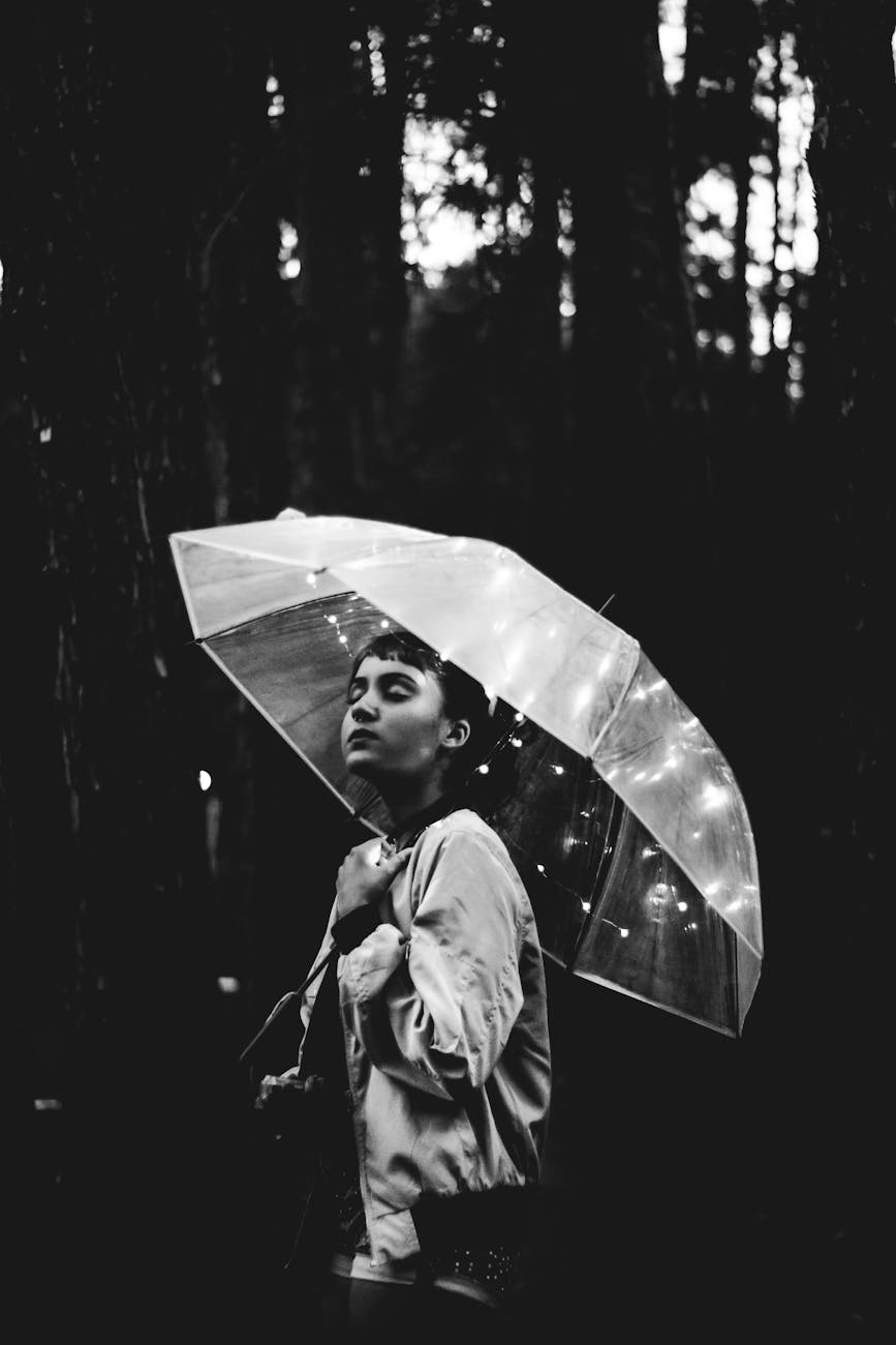 A dramatic black and white portrait of a woman under an umbrella in the rain.