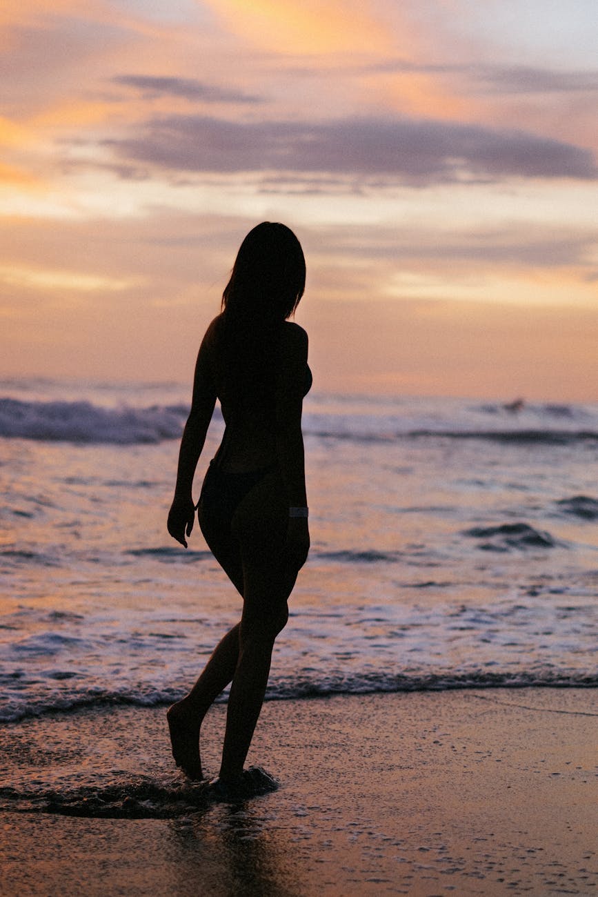 A woman walks along a beach as the sun sets, creating a serene silhouette against the vibrant sky. A woman walks along a beach as the sun sets, creating a serene silhouette against the vibrant sky.