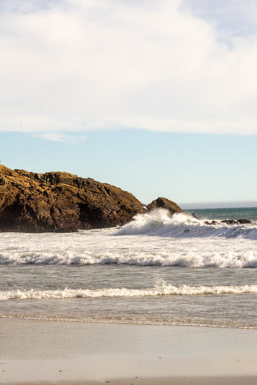 Peaceful scene of waves crashing against rocky shore under clear skies in California, USA.