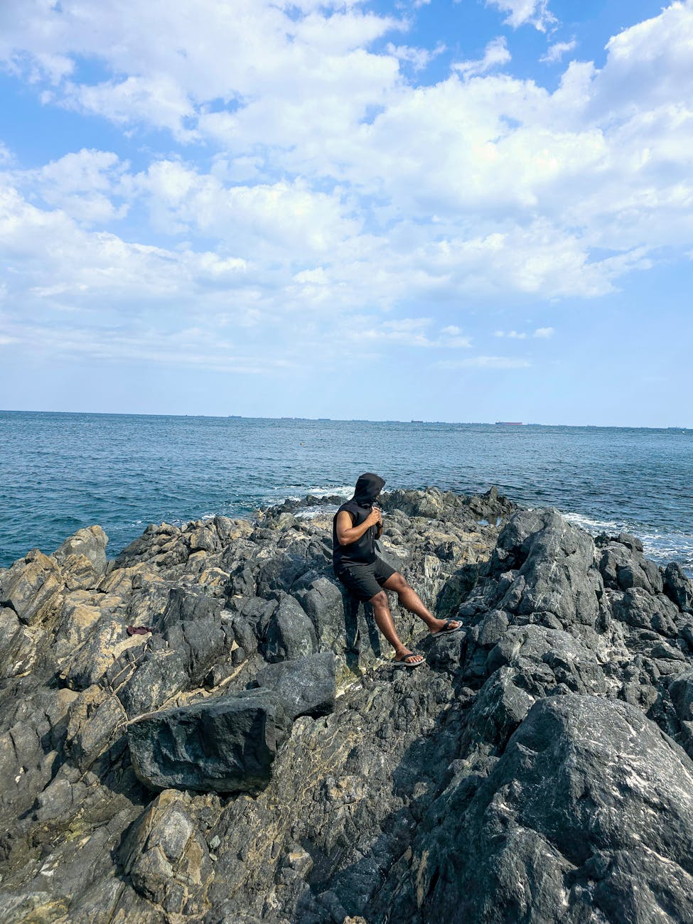 A person standing on rocky shoreline enjoying the expansive ocean view under a partly cloudy sky. A person standing on rocky shoreline enjoying the expansive ocean view under a partly cloudy sky.