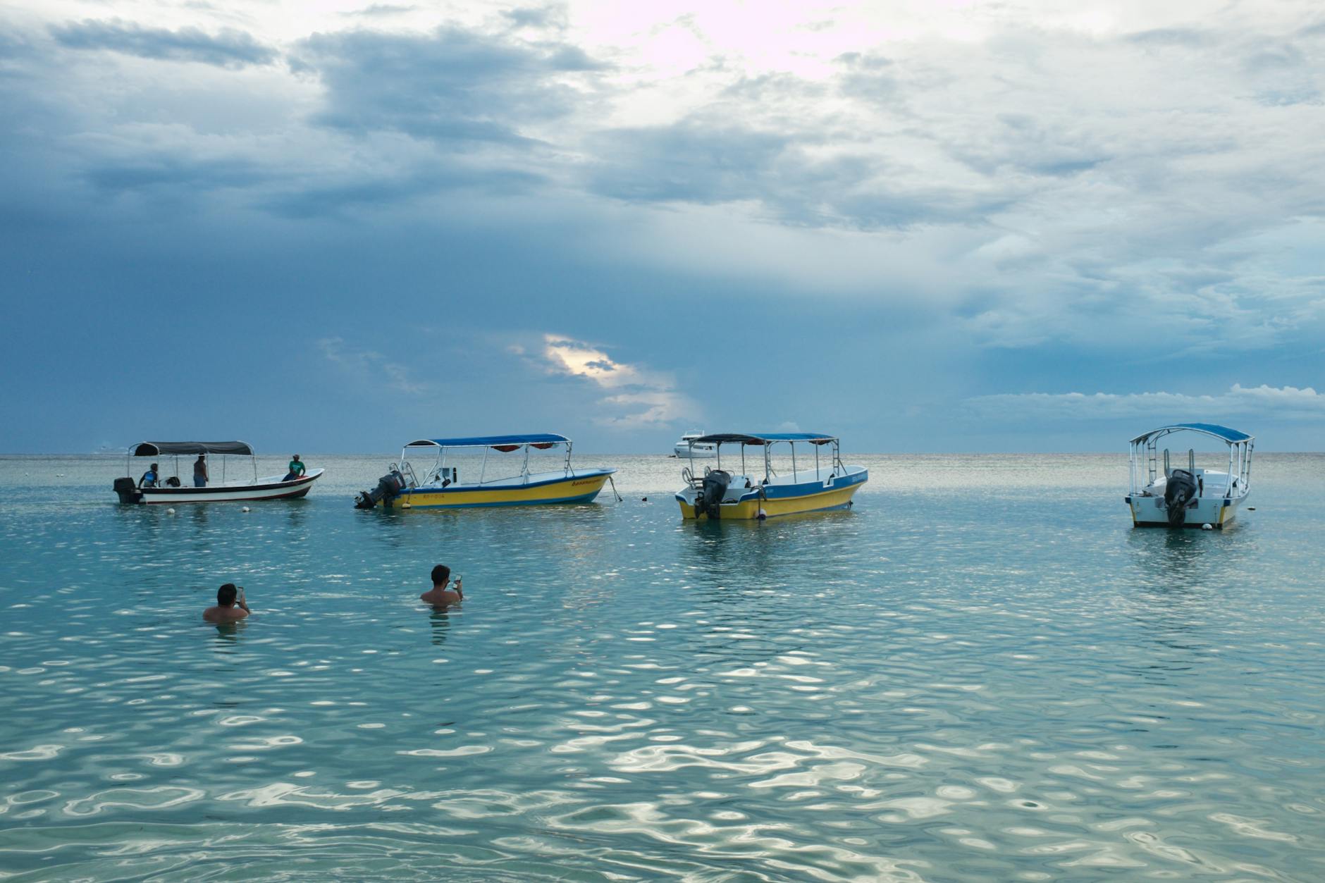 Tranquil ocean scene with boats anchored as swimmers enjoy the calm waters. Tranquil ocean scene with boats anchored as swimmers enjoy the calm waters.