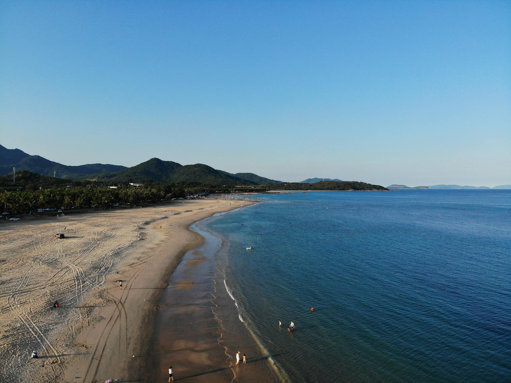A stunning aerial view of a tranquil beach with gentle waves and distant mountains under a blue sky. A stunning aerial view of a tranquil beach with gentle waves and distant mountains under a blue sky.