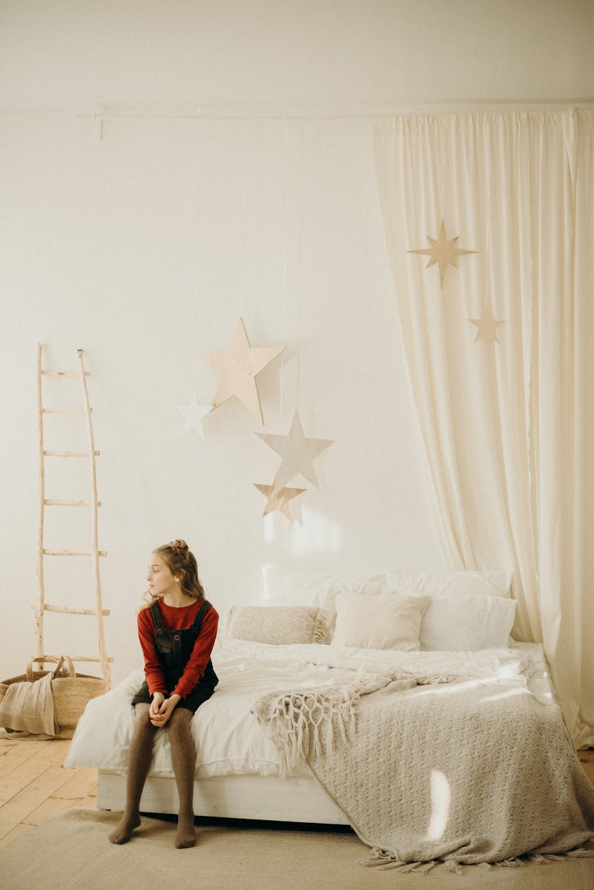 A cozy bedroom with festive decorations and a young girl sitting on the bed. A cozy bedroom with festive decorations and a young girl sitting on the bed.