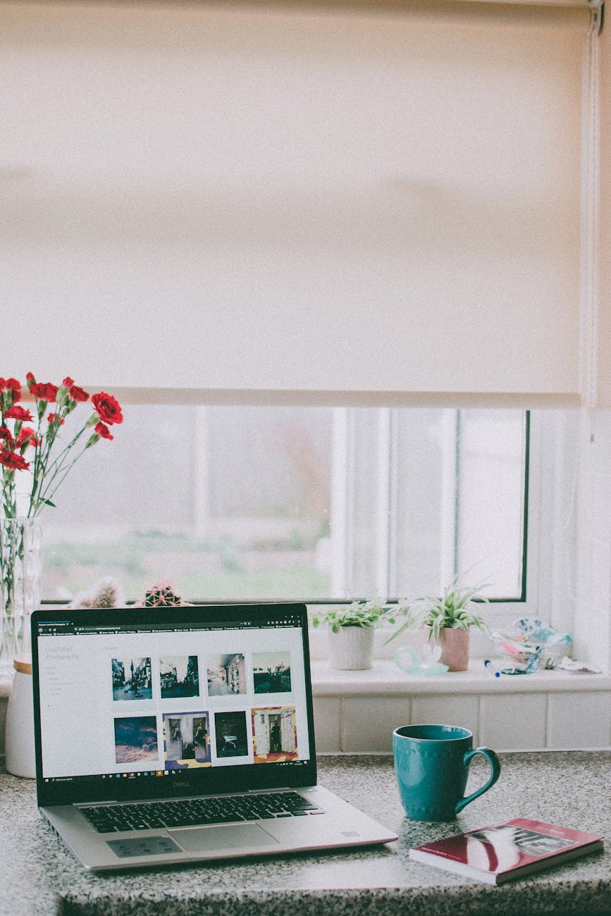 A cozy home office setup with a laptop, coffee mug, and flowers by a sunlit window, ideal for remote work. A cozy home office setup with a laptop, coffee mug, and flowers by a sunlit window, ideal for remote work.