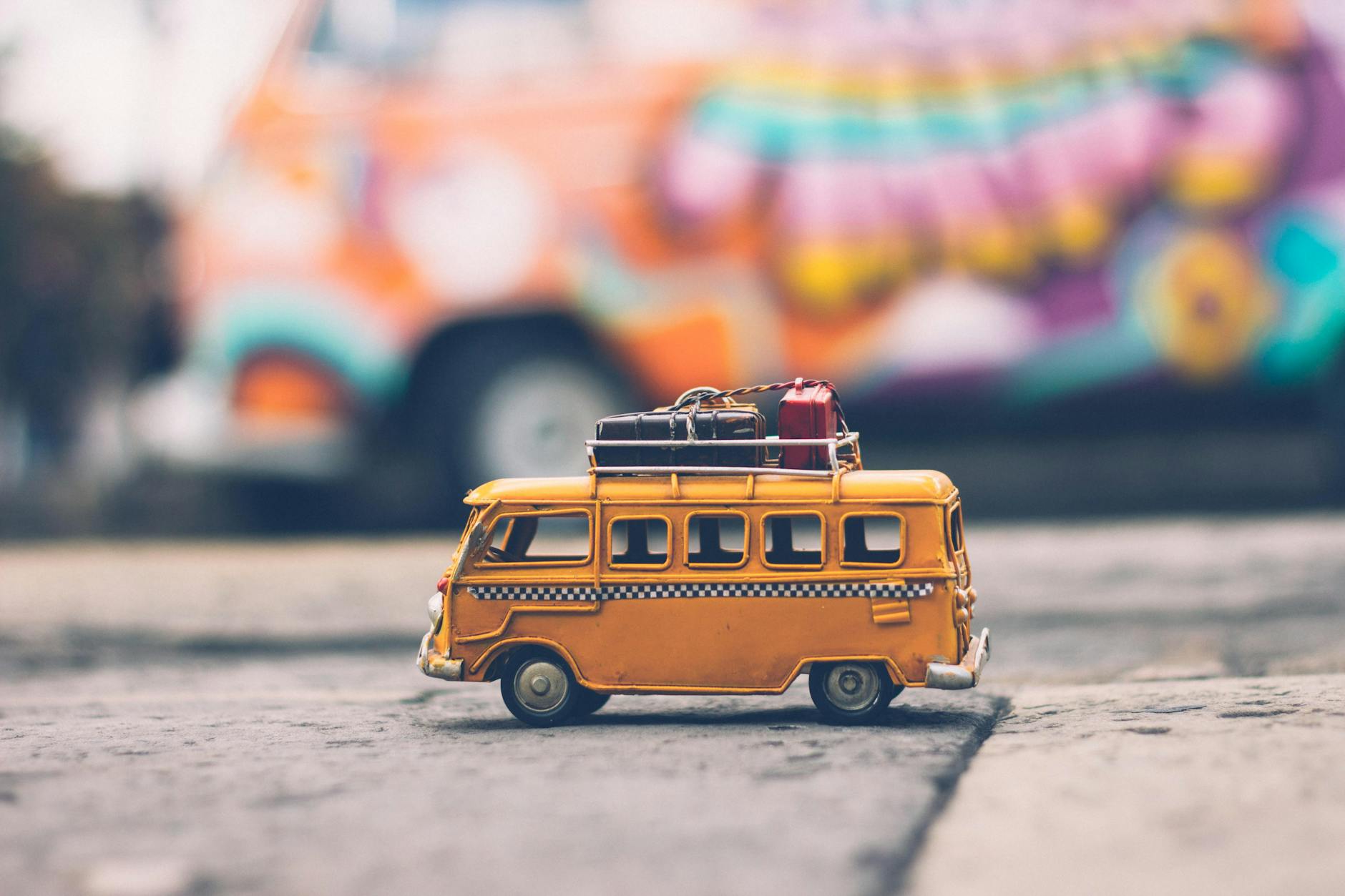 Close-up of a toy Volkswagen van with luggage, set against a colorful street backdrop, evoking summer travel vibes. Close-up of a toy Volkswagen van with luggage, set against a colorful street backdrop, evoking summer travel vibes.
