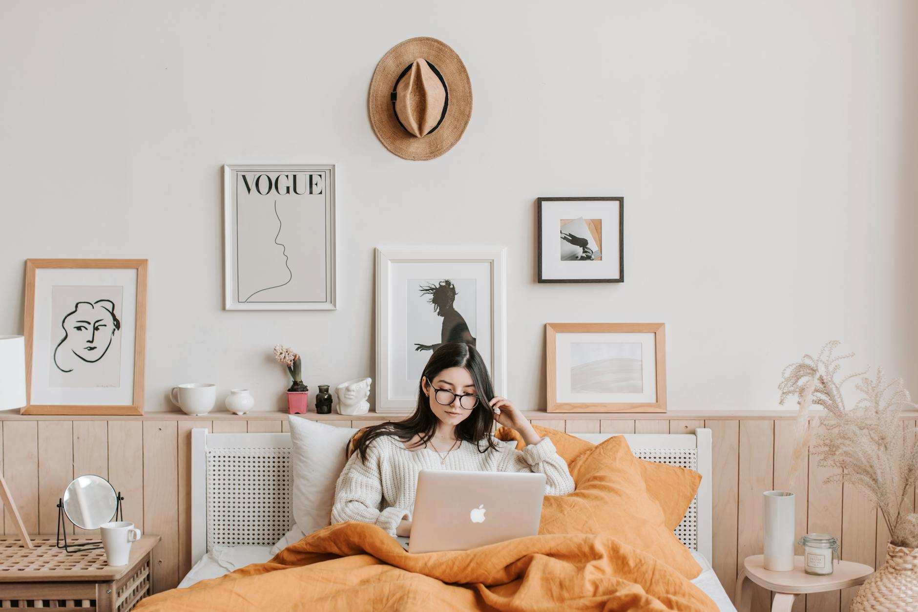 Young woman in cozy bedroom using a laptop, surrounded by stylish decor and art. Young woman in cozy bedroom using a laptop, surrounded by stylish decor and art.