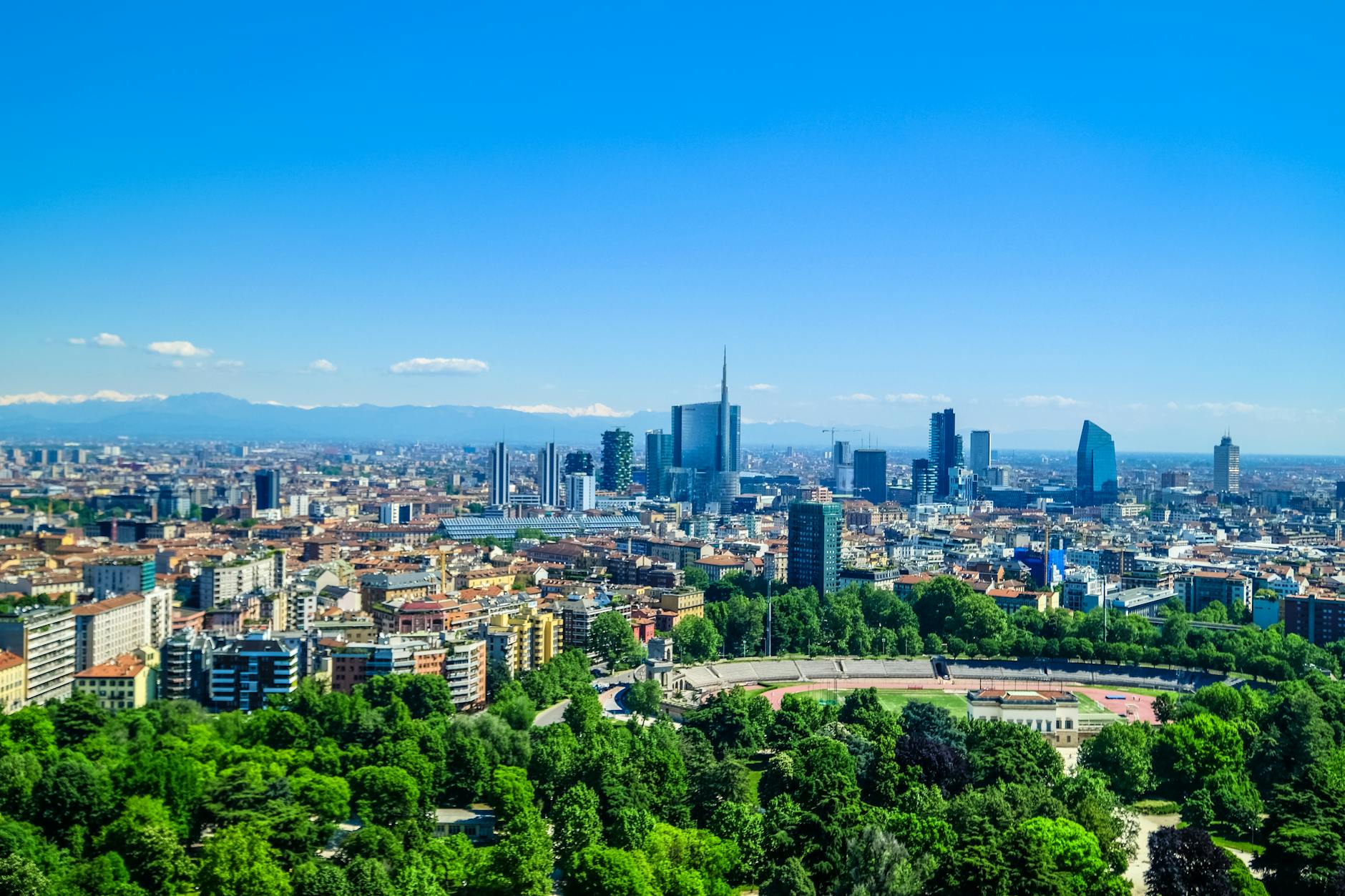 Panoramic view of Milan’s skyline featuring modern skyscrapers and lush greenery under a clear blue sky. Panoramic view of Milan’s skyline featuring modern skyscrapers and lush greenery under a clear blue sky.