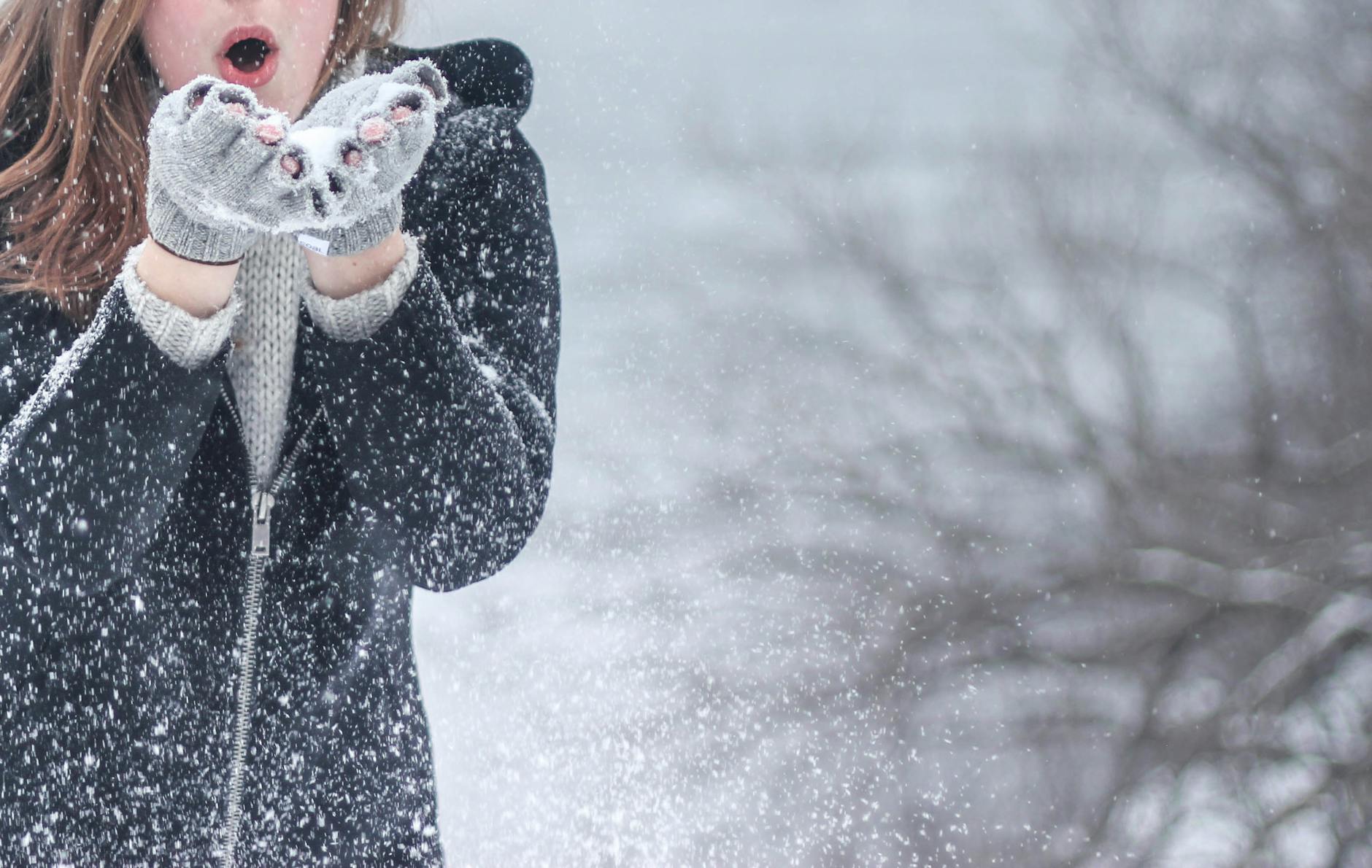Woman in cozy winter clothing blowing snowflakes with excitement outdoors in a snowy setting. Woman in cozy winter clothing blowing snowflakes with excitement outdoors in a snowy setting.