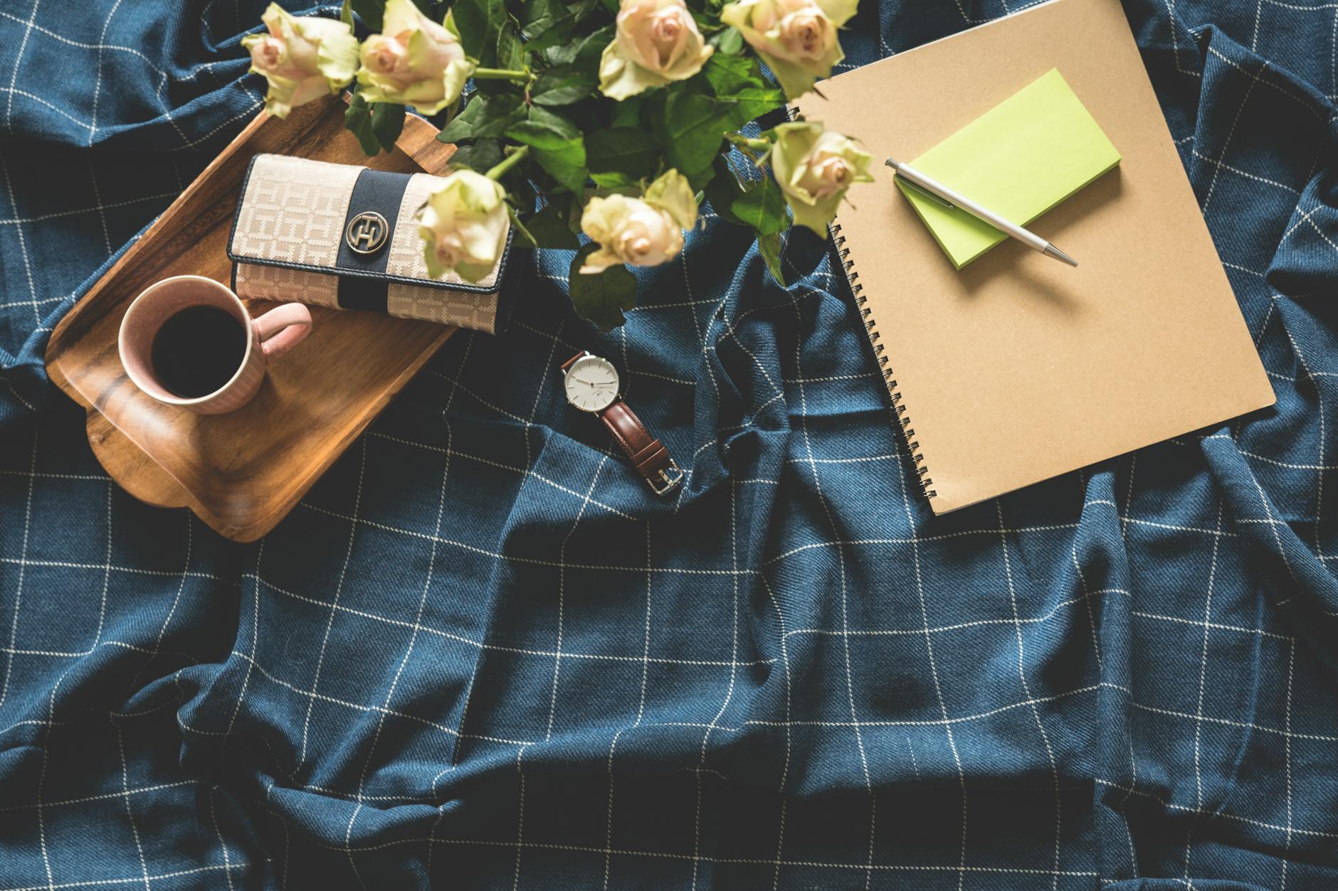 A cozy flatlay showing coffee, roses, notebook, and watch on a checkered blanket. A cozy flatlay showing coffee, roses, notebook, and watch on a checkered blanket.
