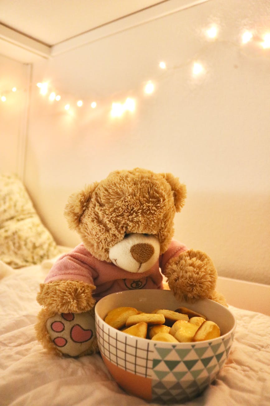 A cozy scene with a teddy bear and a bowl of cookies in a warmly lit bedroom.