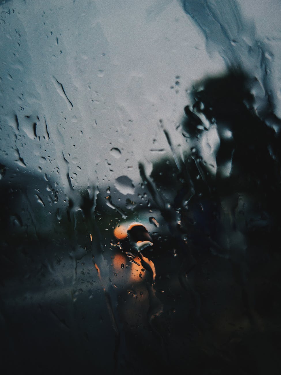 Raindrops on a window with blurred street lights creating a moody scene.