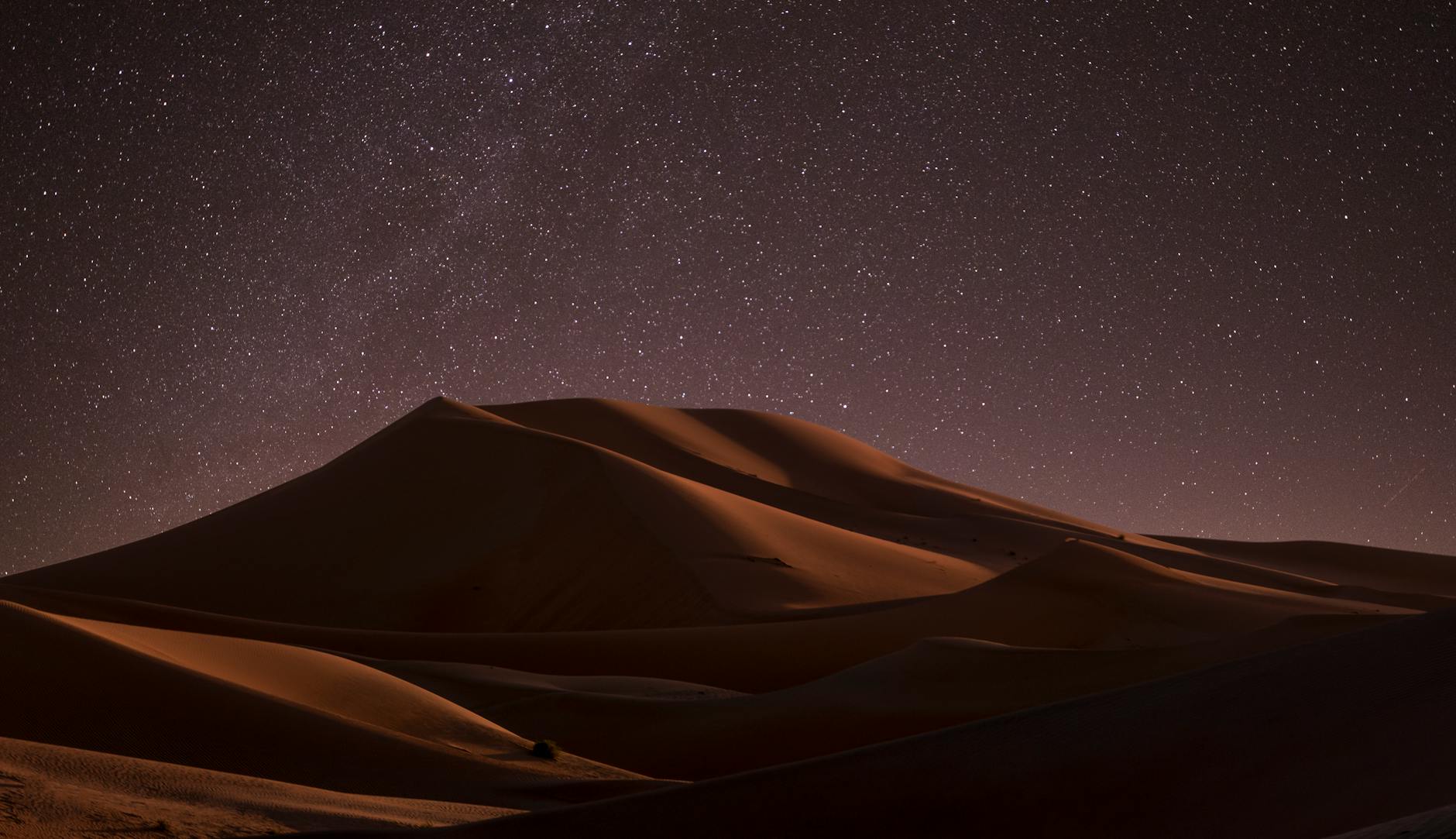 A captivating view of starlit sky above serene desert dunes at night, offering a tranquil escape.
