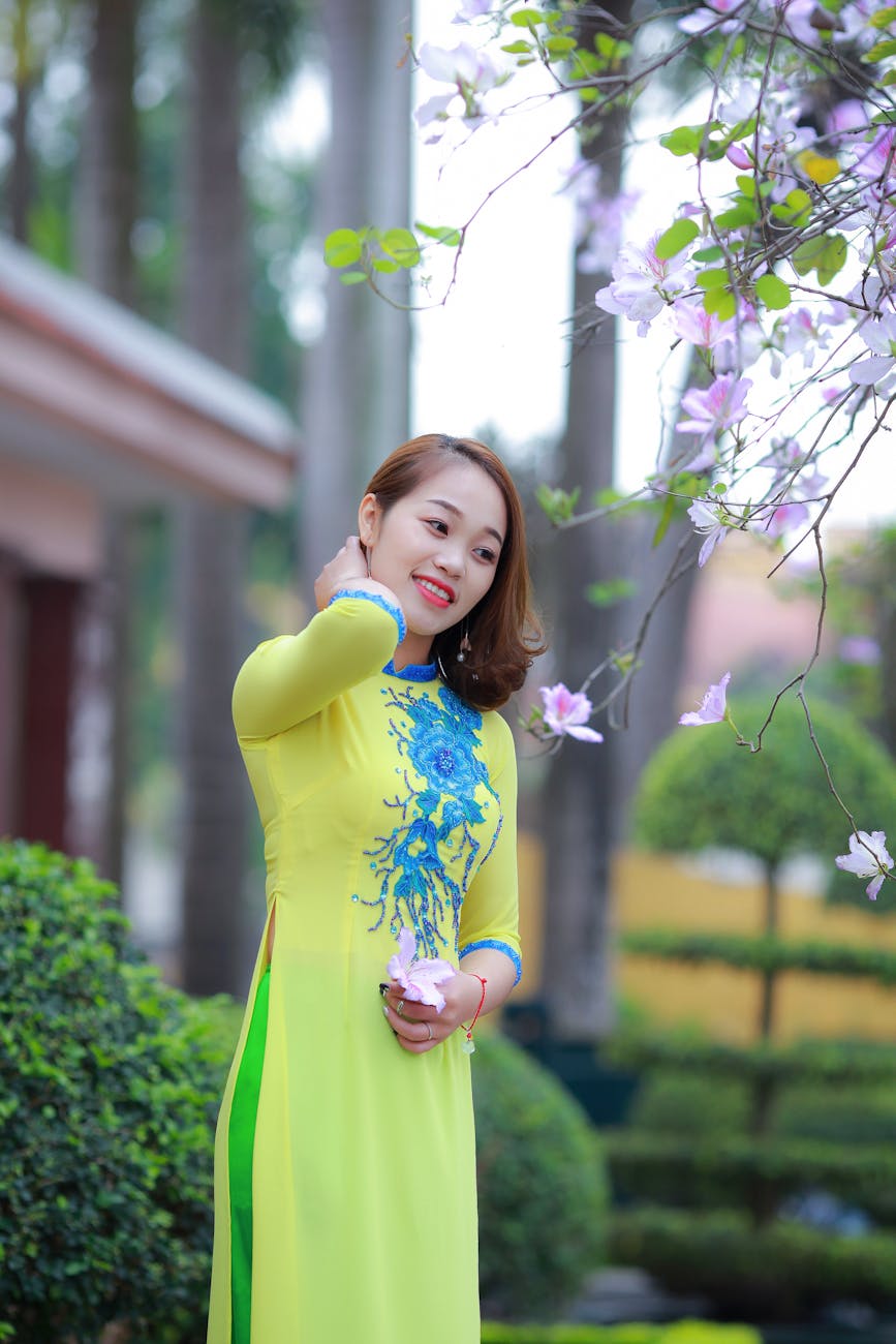 Young woman in ao dai smiles holding blossoms outdoors on a sunny day. Young woman in ao dai smiles holding blossoms outdoors on a sunny day.